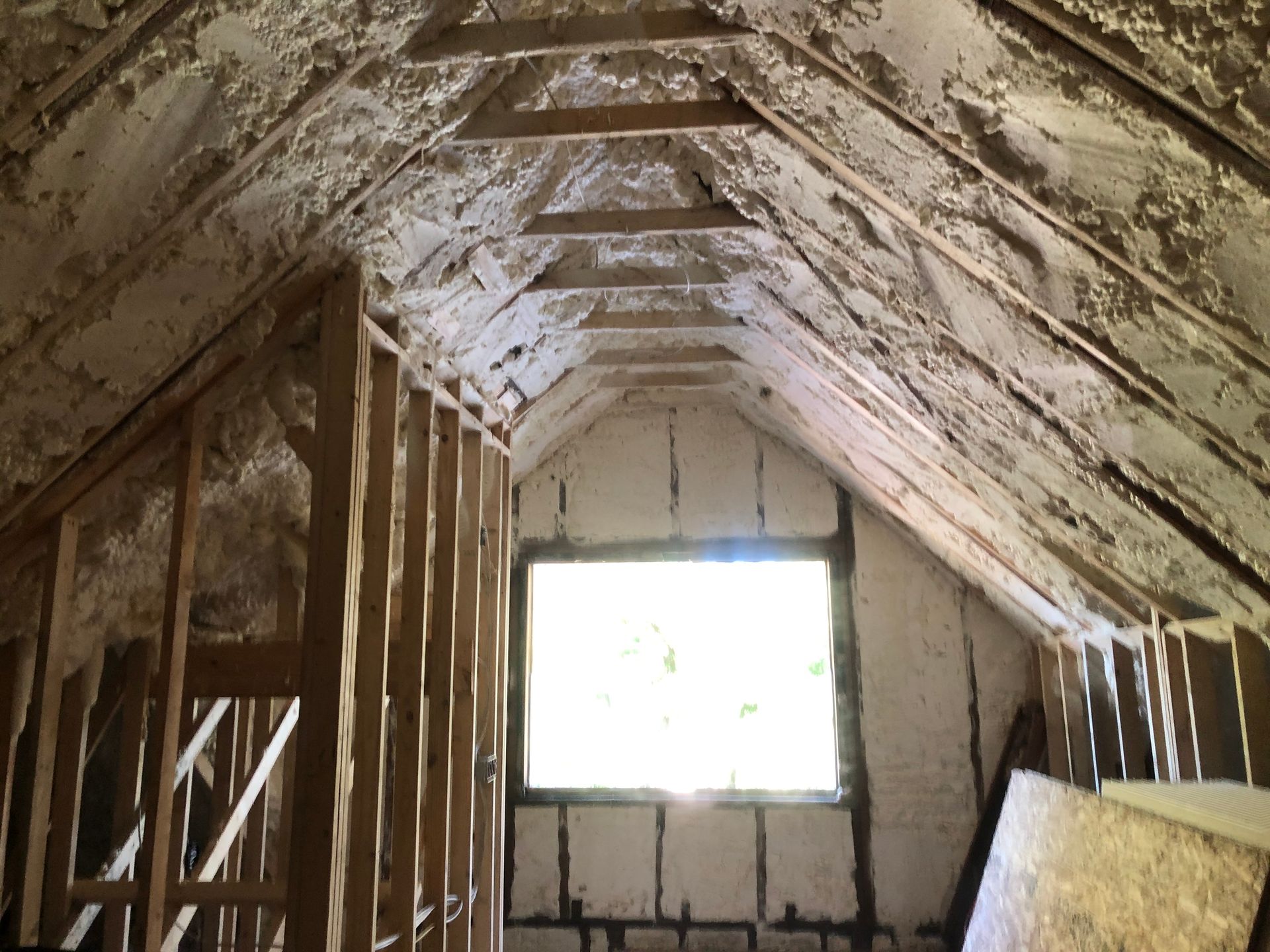 Abandoned attic under renovation with exposed rafters, insulation, and a bright window at the end.