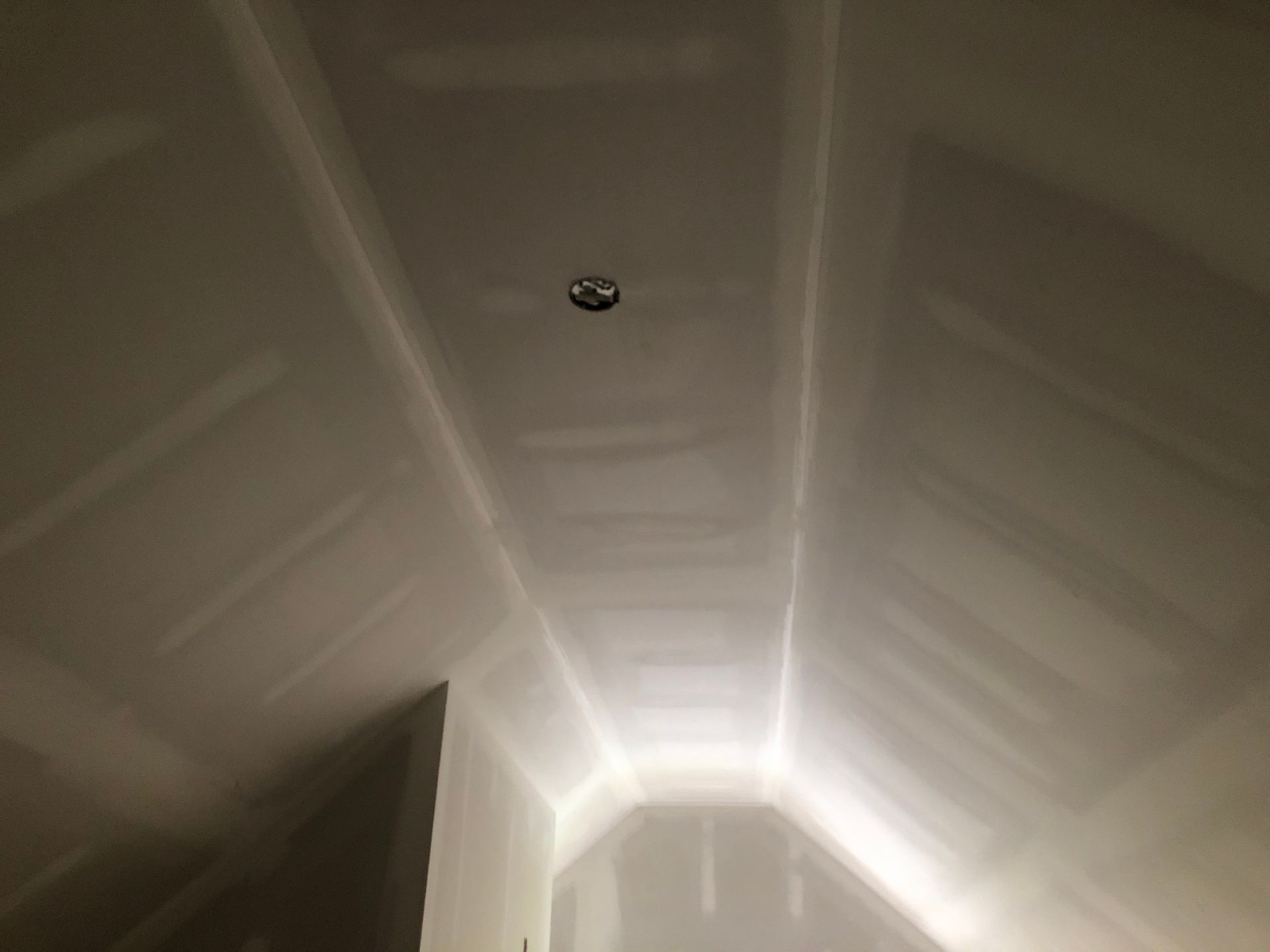 Interior of an unfinished white hallway ceiling with a recessed light at the far end