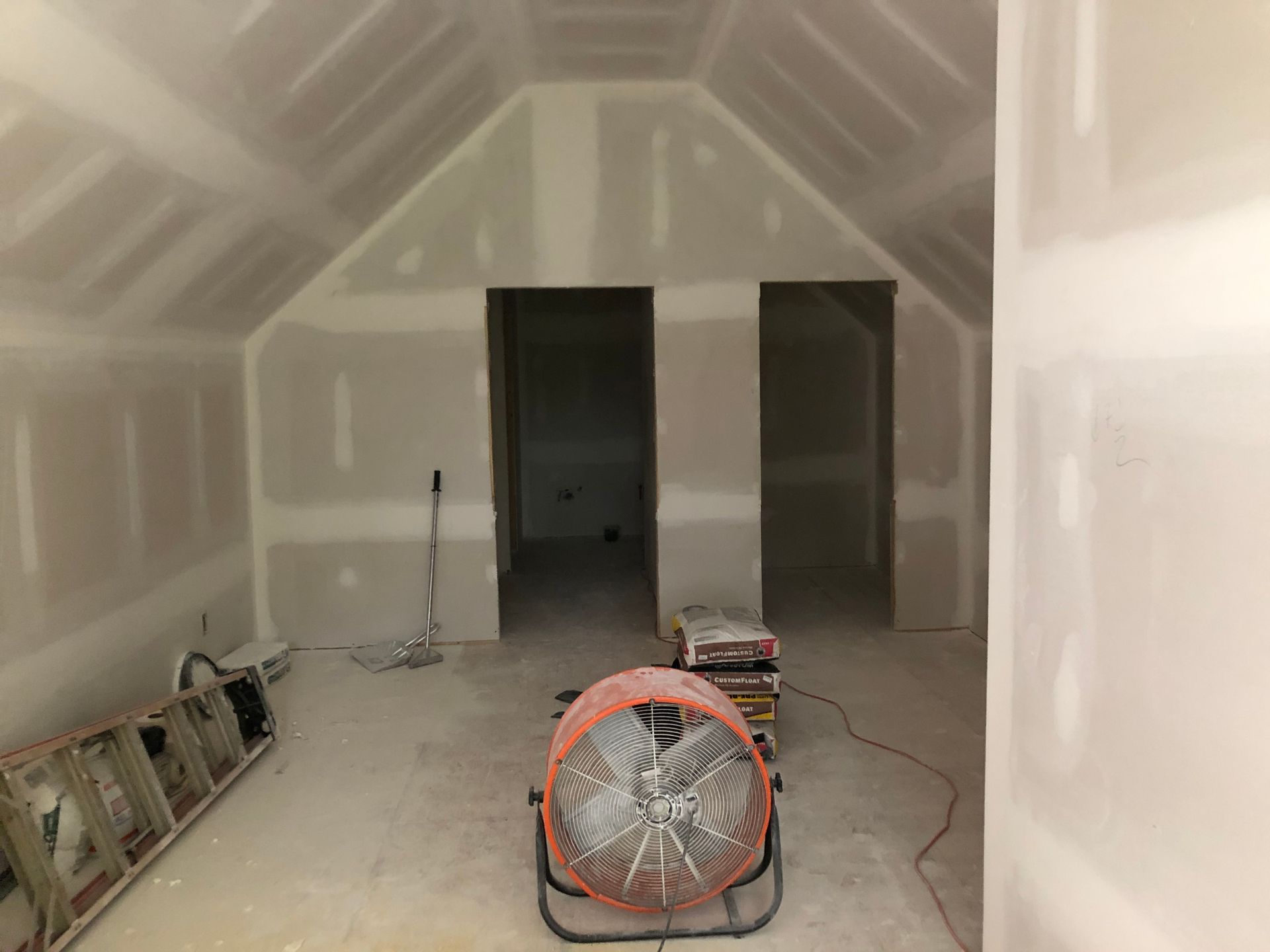 Unfinished room with drywall, two open doorways, a fan, ladder, and construction tools on the floor