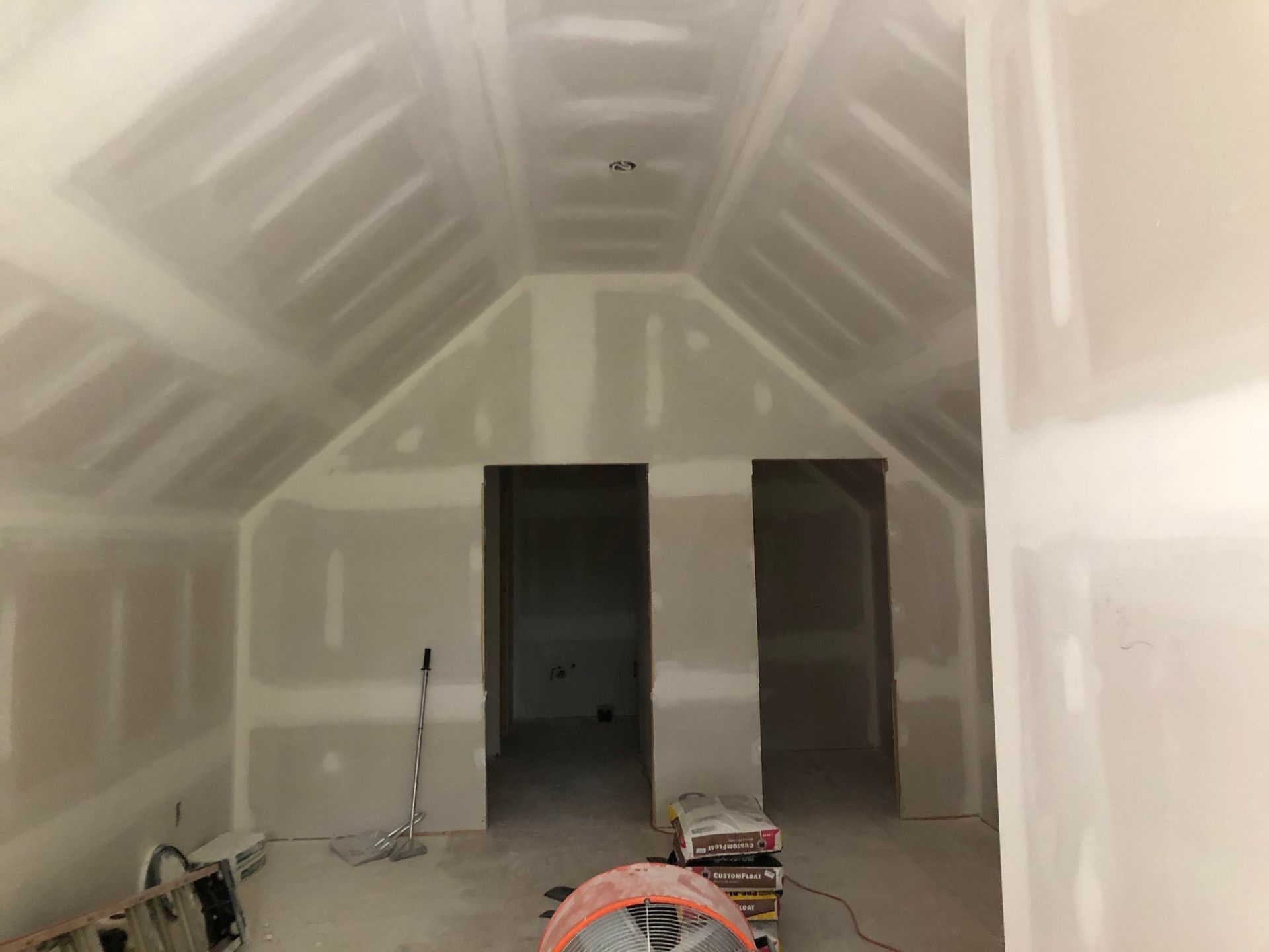 Unfinished attic with drywall, exposed ceiling beams, and construction tools on the floor.