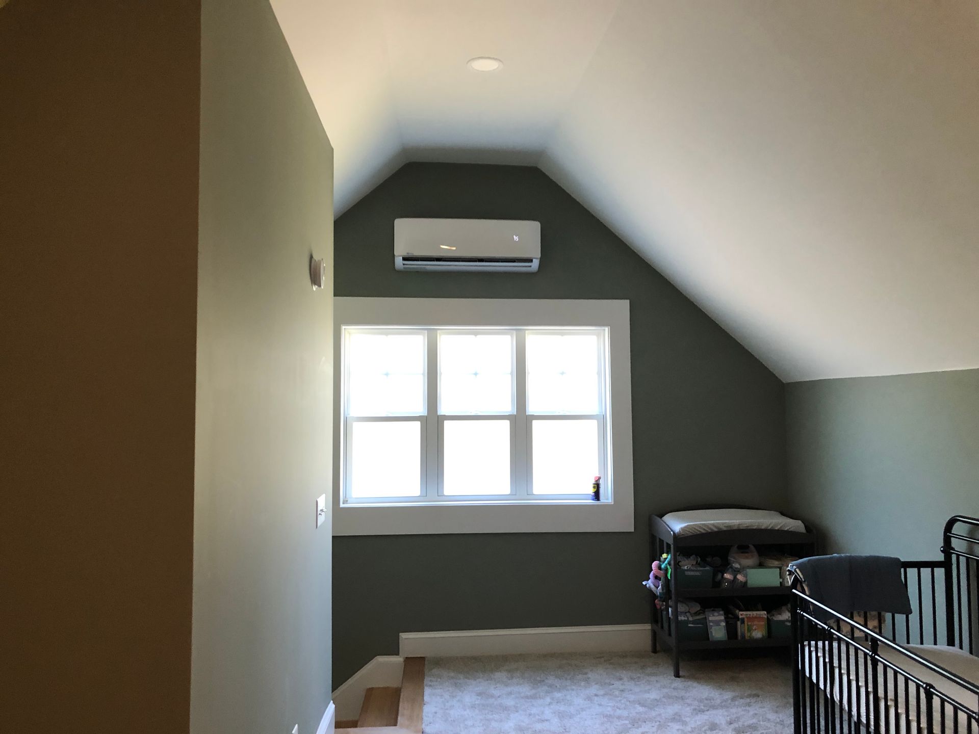 Spare bedroom with sloped ceiling, window, wall-mounted AC, and a bed frame by the right wall.