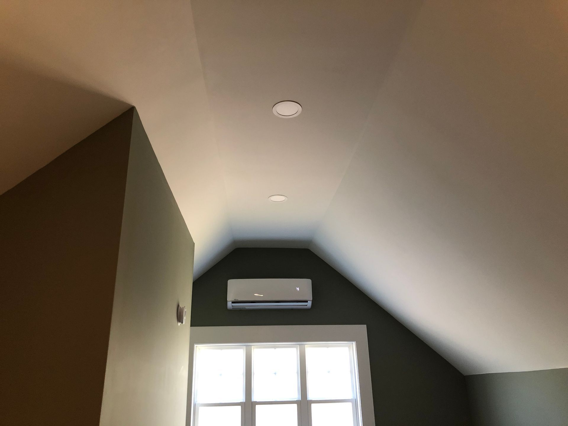 Attic room with sloped ceiling, wall-mounted air conditioner, and window with bright light