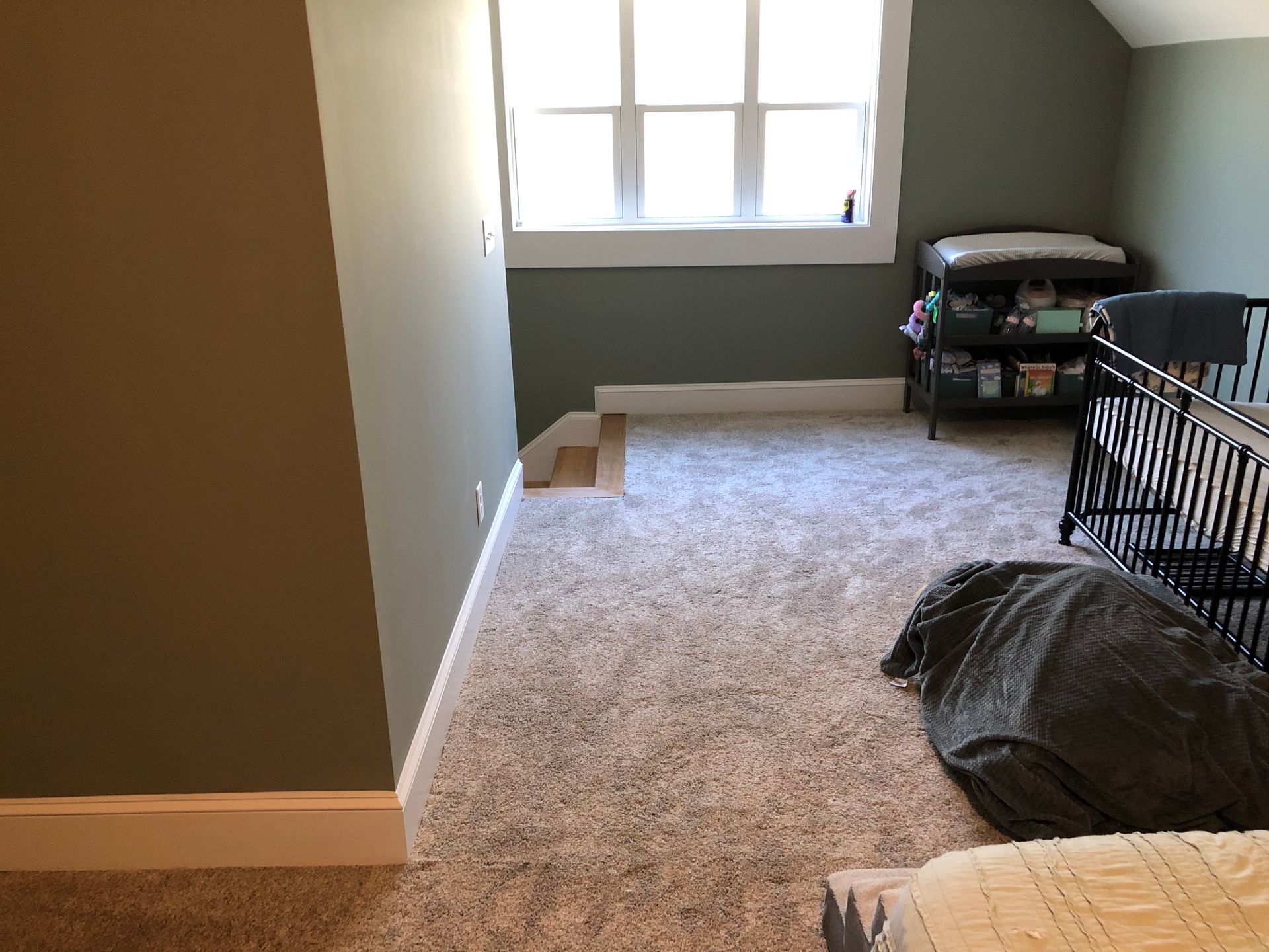 Empty carpeted room with a window, gray walls, and a few storage bins and items along the right side.
