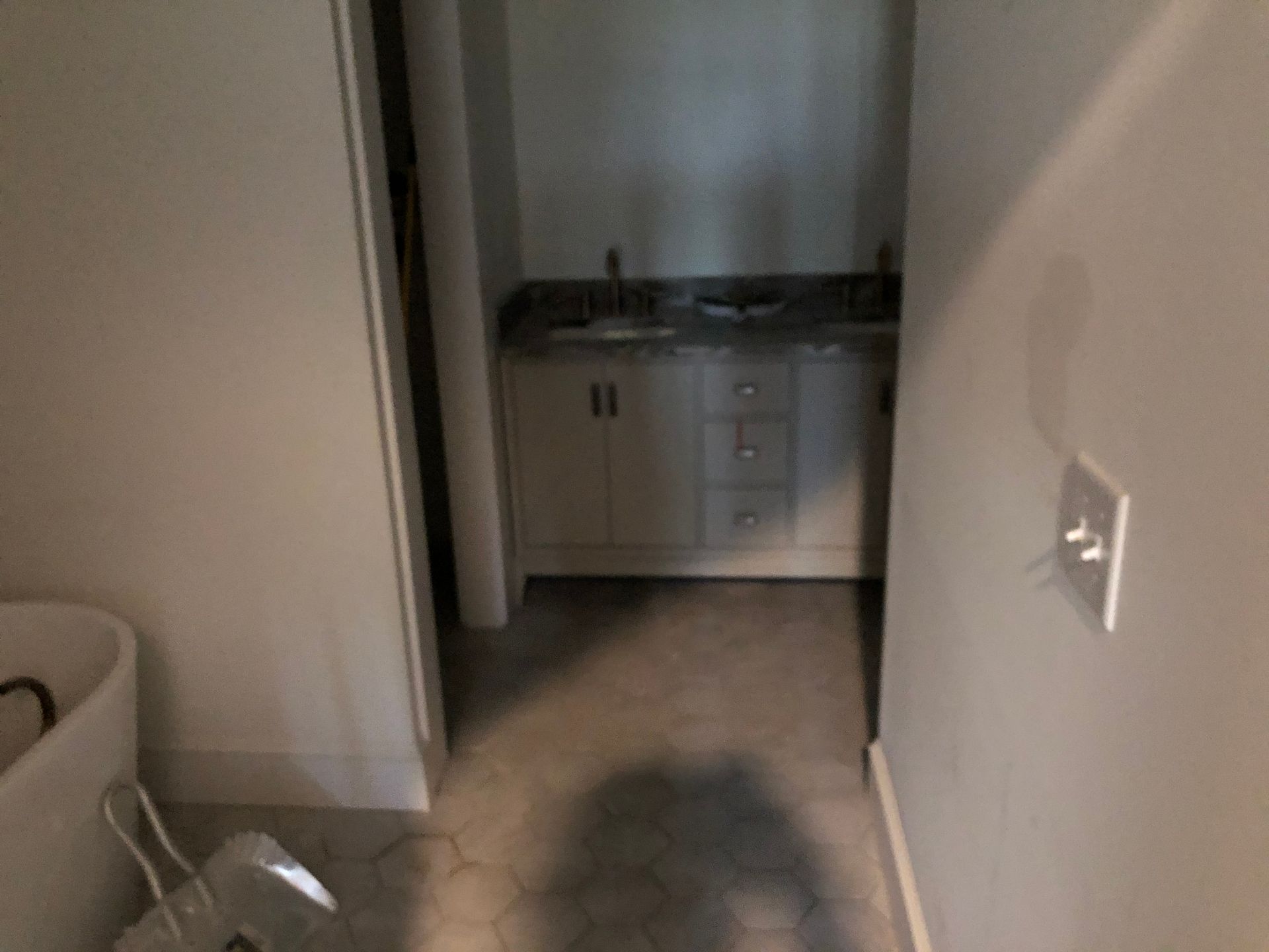 Narrow hallway leading to a small kitchen with white cabinets and a dark countertop.