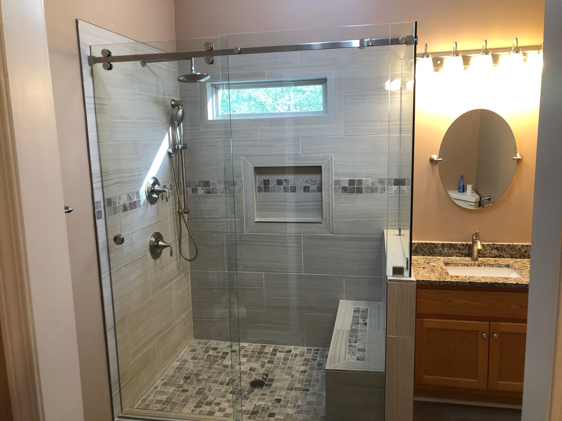 Glass shower stall beside a vanity and mirror in a tiled bathroom