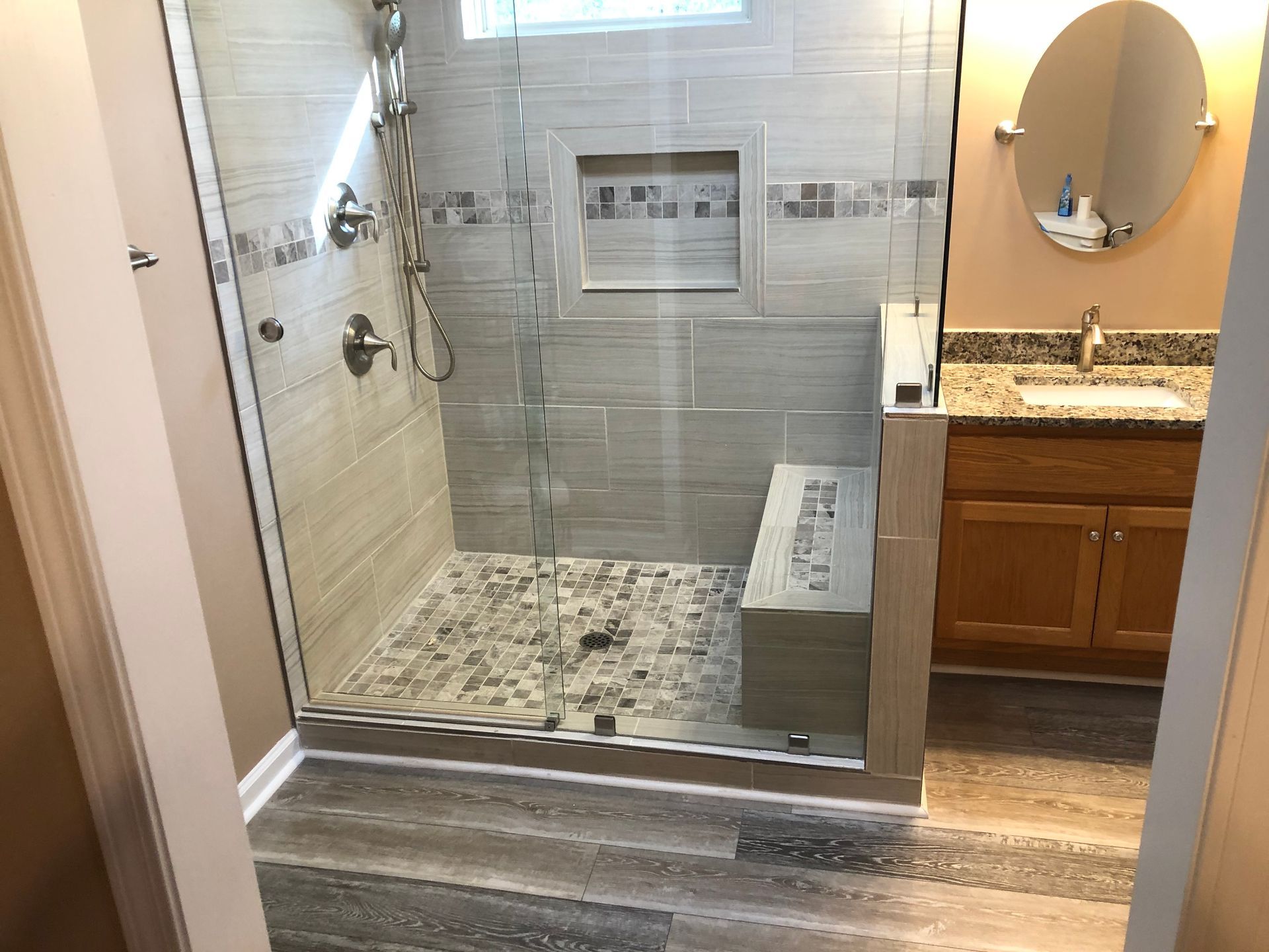 Bathroom with a curbless glass shower, gray tile walls, pebble floor, and granite vanity visible on the right.