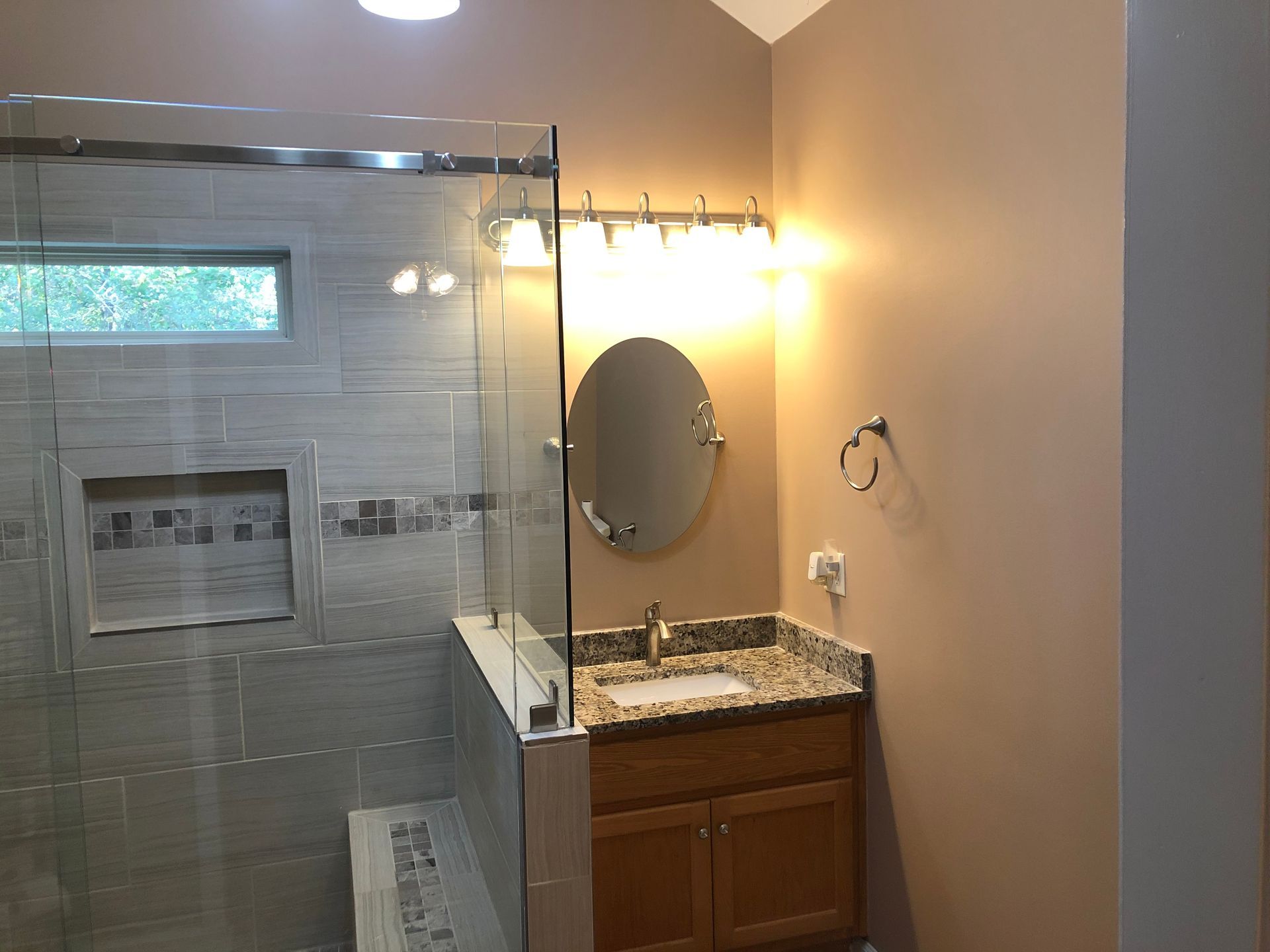 Bathroom vanity with round mirror, granite counter, and glass shower enclosure in a softly lit room