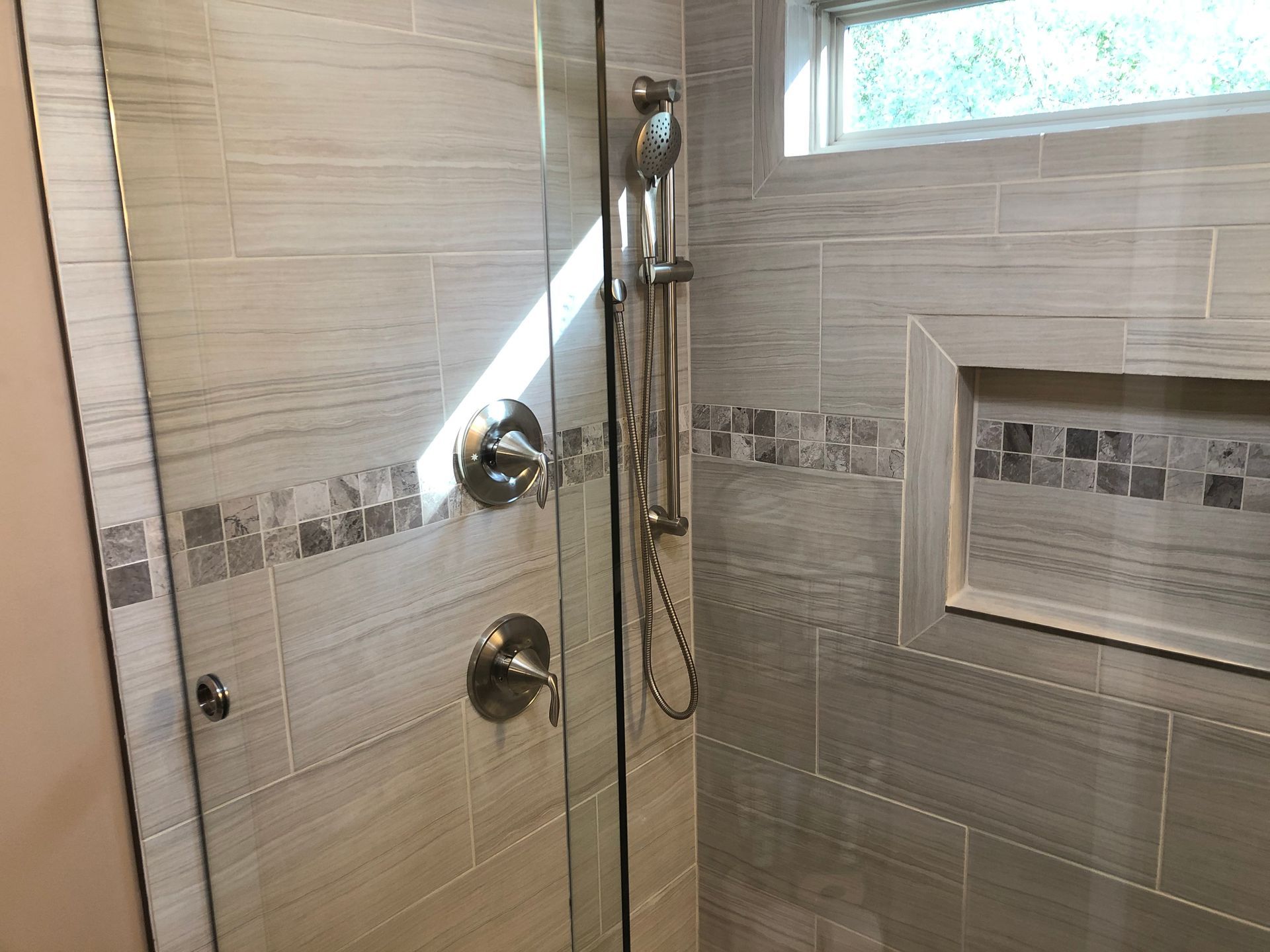 Modern tiled shower with glass door, chrome fixtures, and recessed shelf