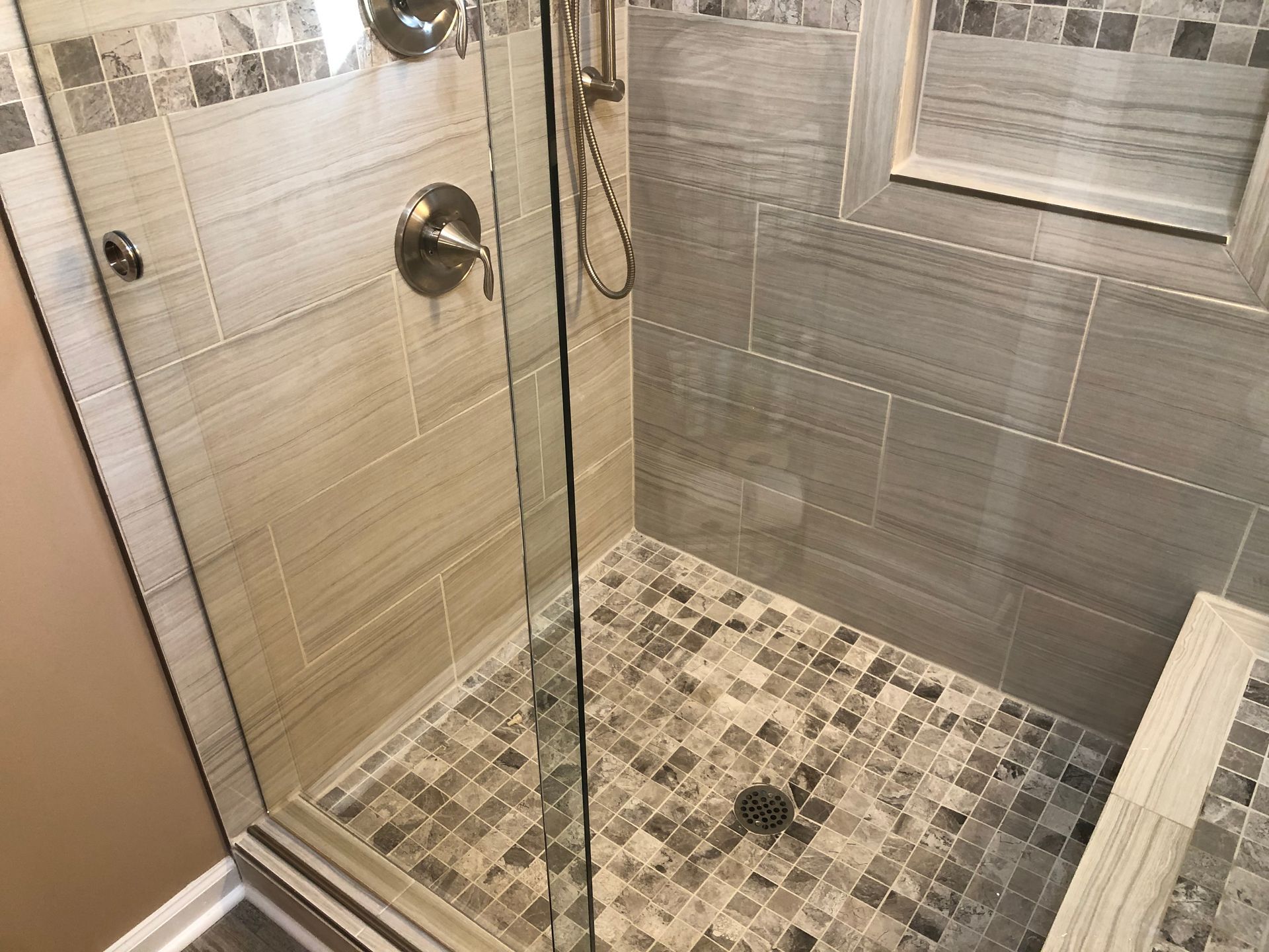 Modern tiled walk-in shower with glass door and mosaic floor tiles