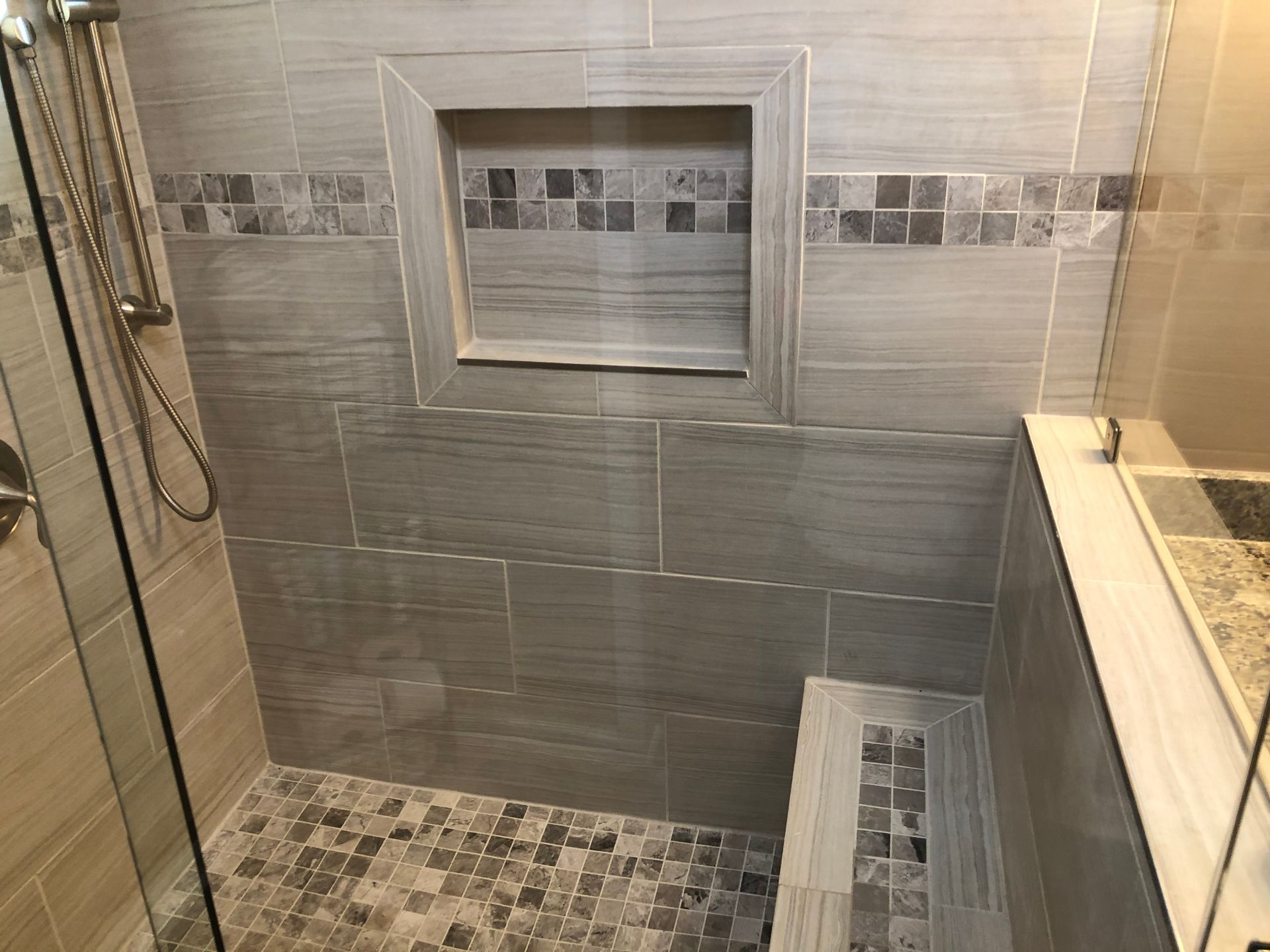 Modern tiled walk-in shower with a glass partition, built-in niche, and mosaic floor accents