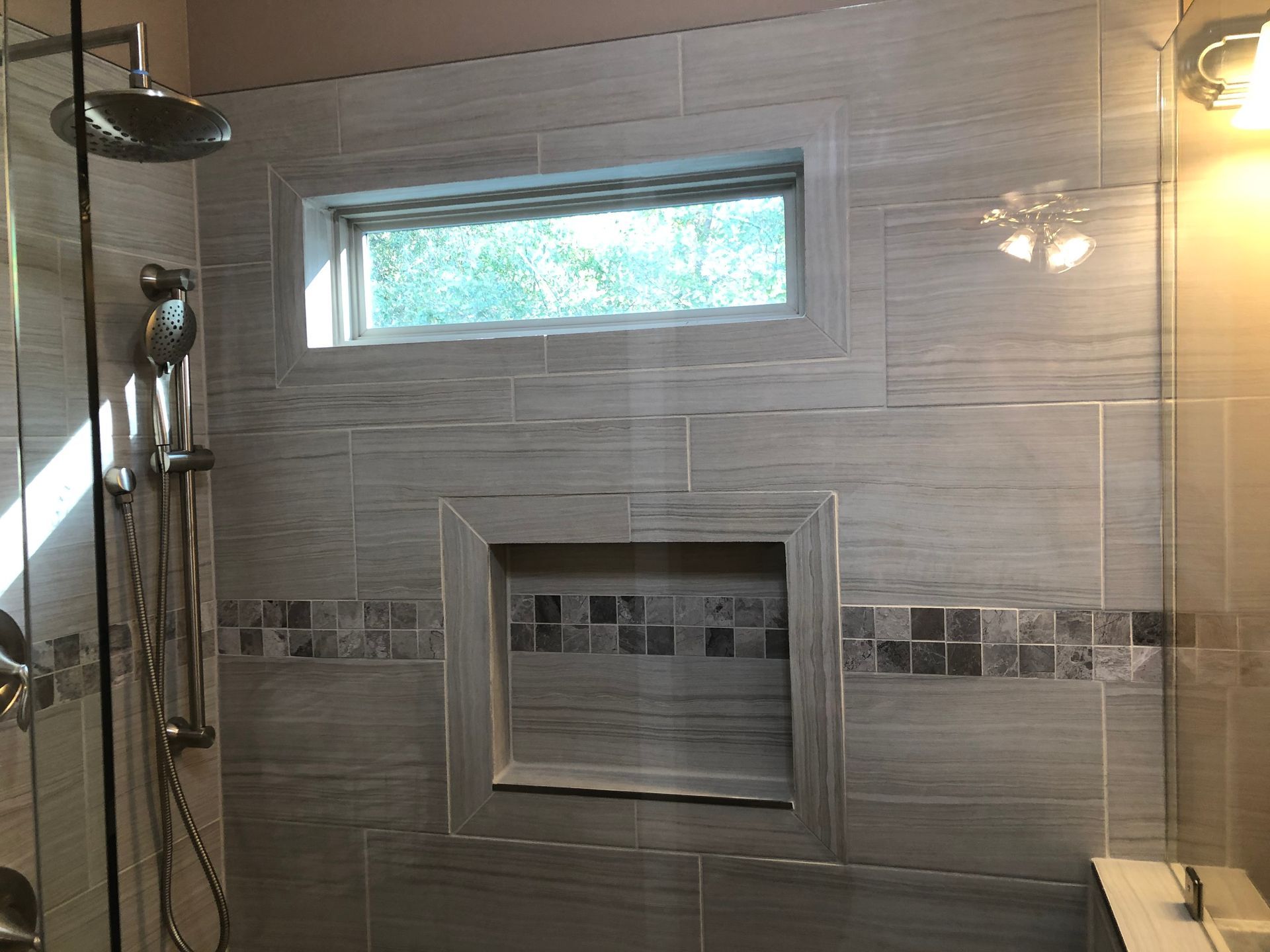 Glass shower with tiled walls, a narrow window, and a built-in shelf niche.