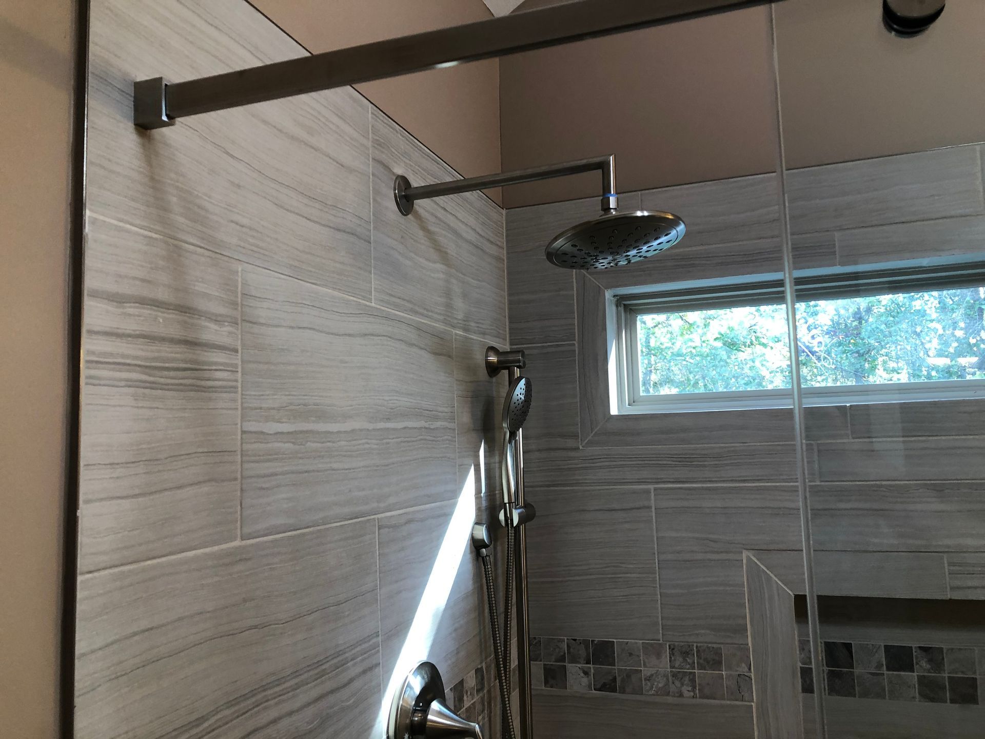 Modern tiled shower with rainfall showerhead, glass window, and overhead grab bar