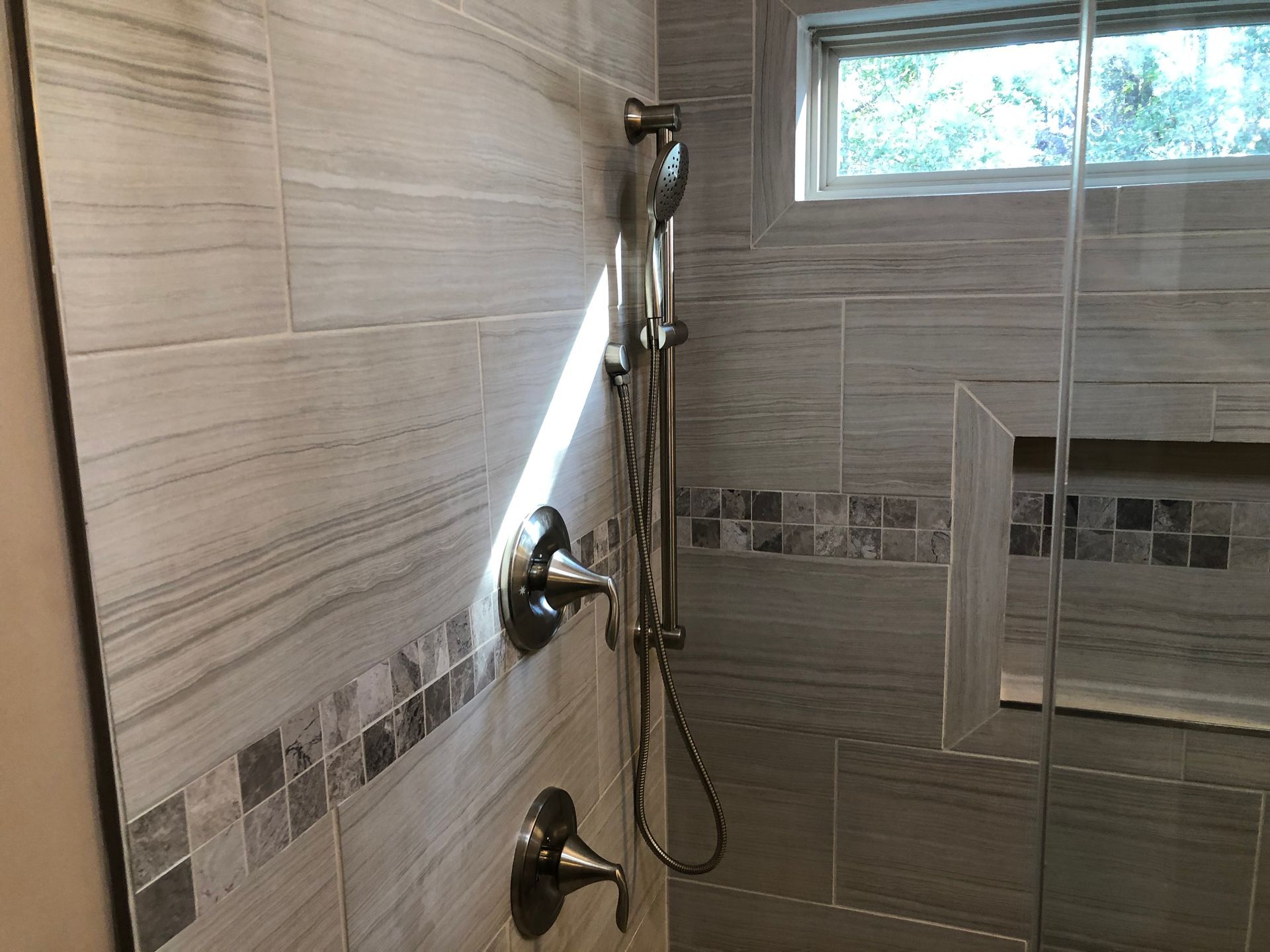 Walk-in shower with tiled walls, glass door, and chrome shower fixtures with handheld sprayer