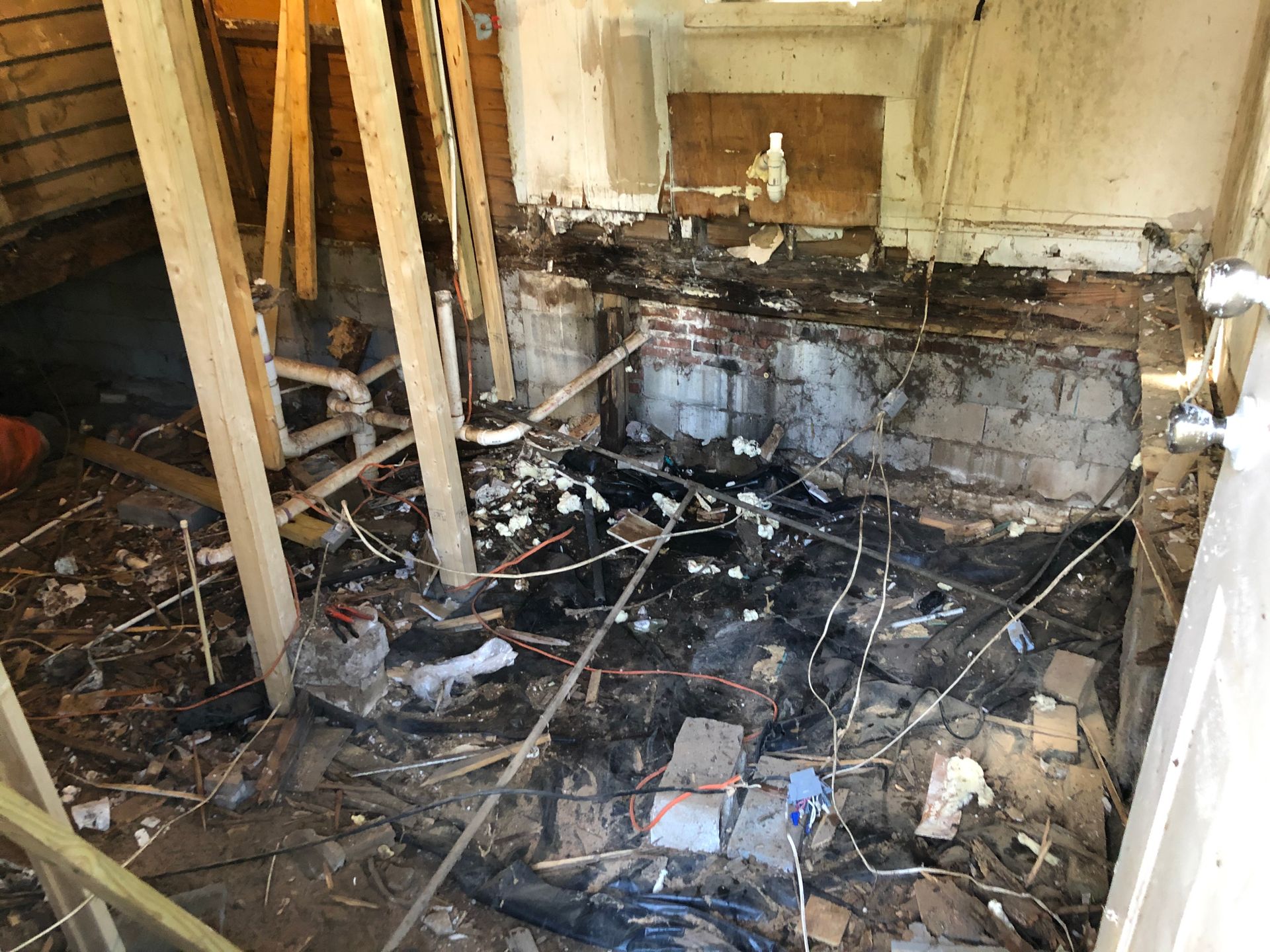 Burned, debris-filled room with charred walls, collapsed floor, and scattered rubble and wires