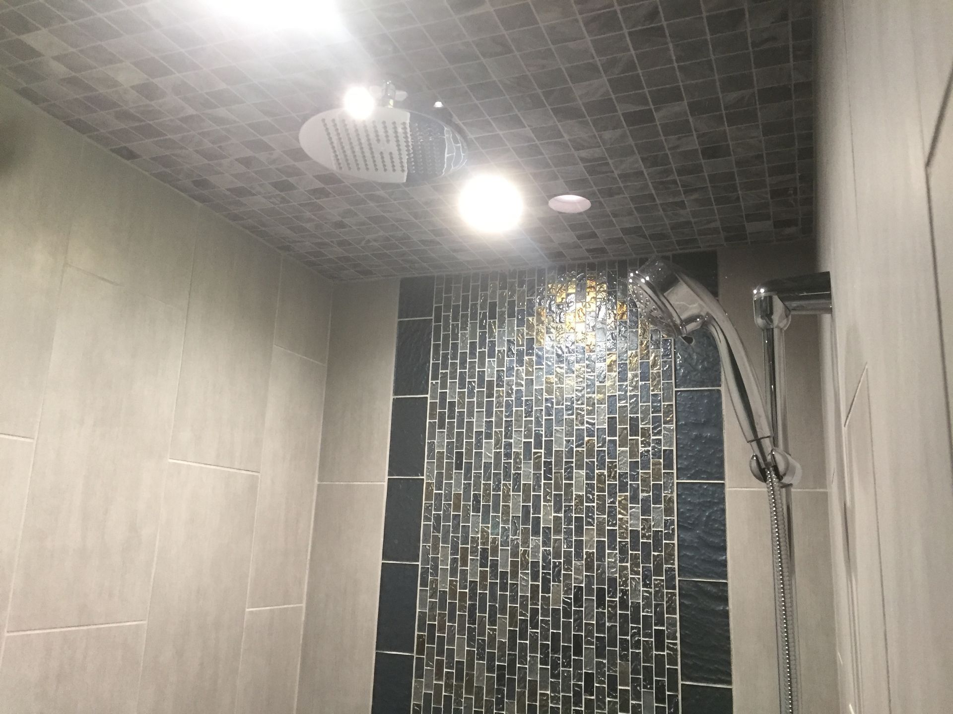 Modern bathroom shower with gray walls, black mosaic tile, and a ceiling showerhead running water
