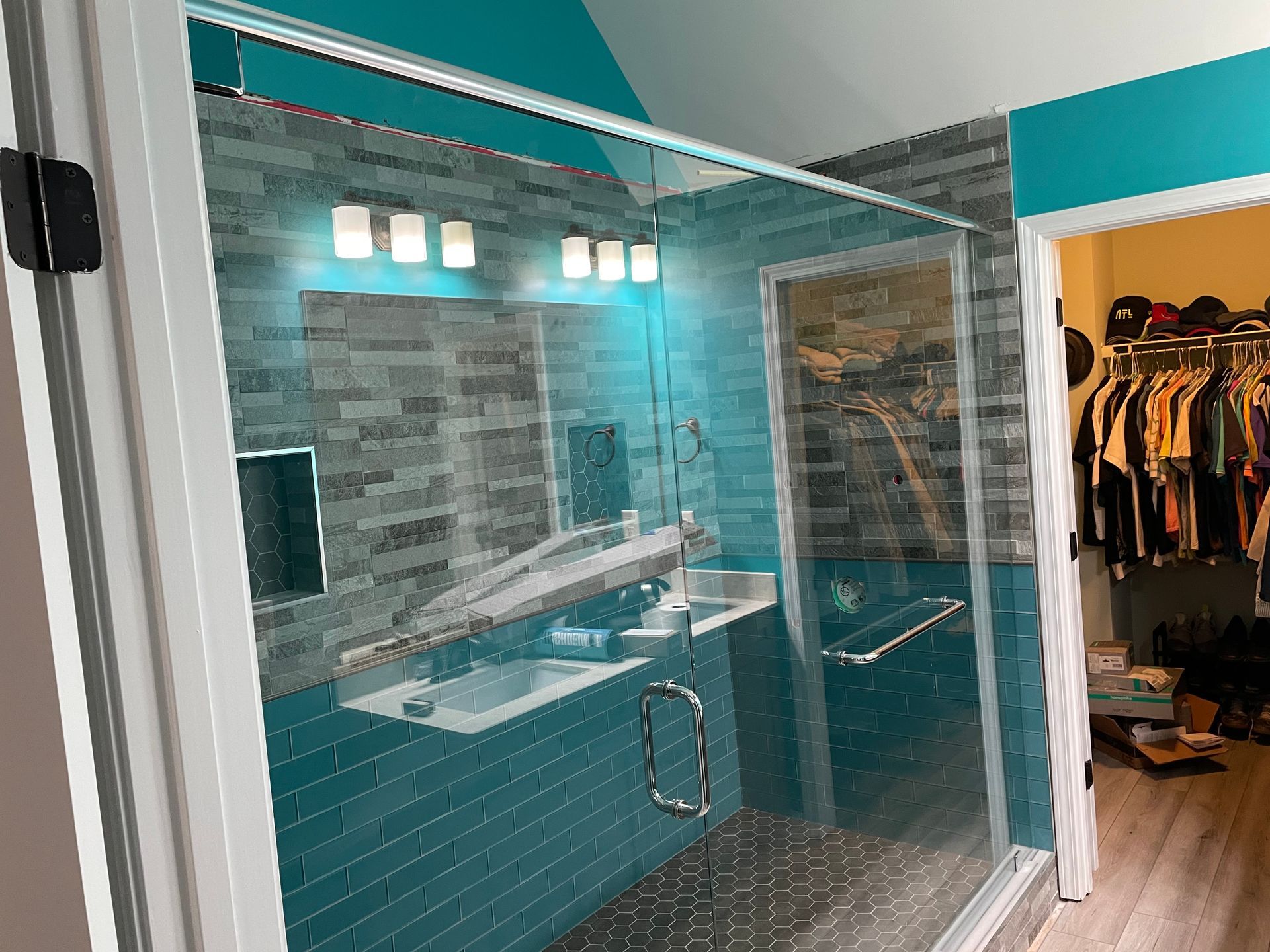 Modern bathroom with glass shower enclosure, turquoise tile, sink vanity, and open closet area