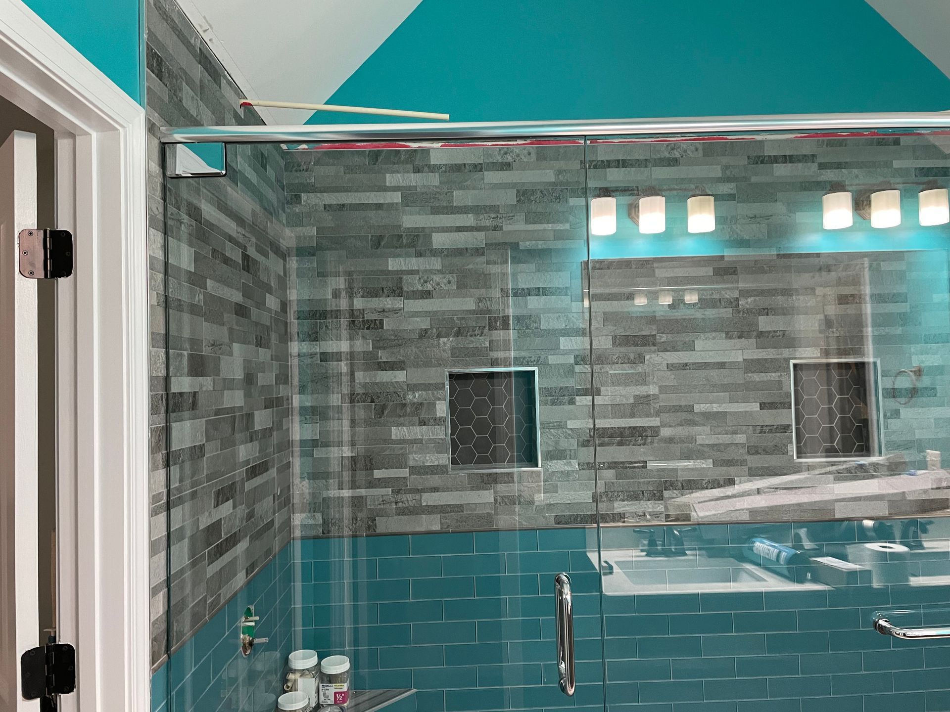 Modern bathroom shower with teal tile, gray stone wall, and glass shelf with toiletries