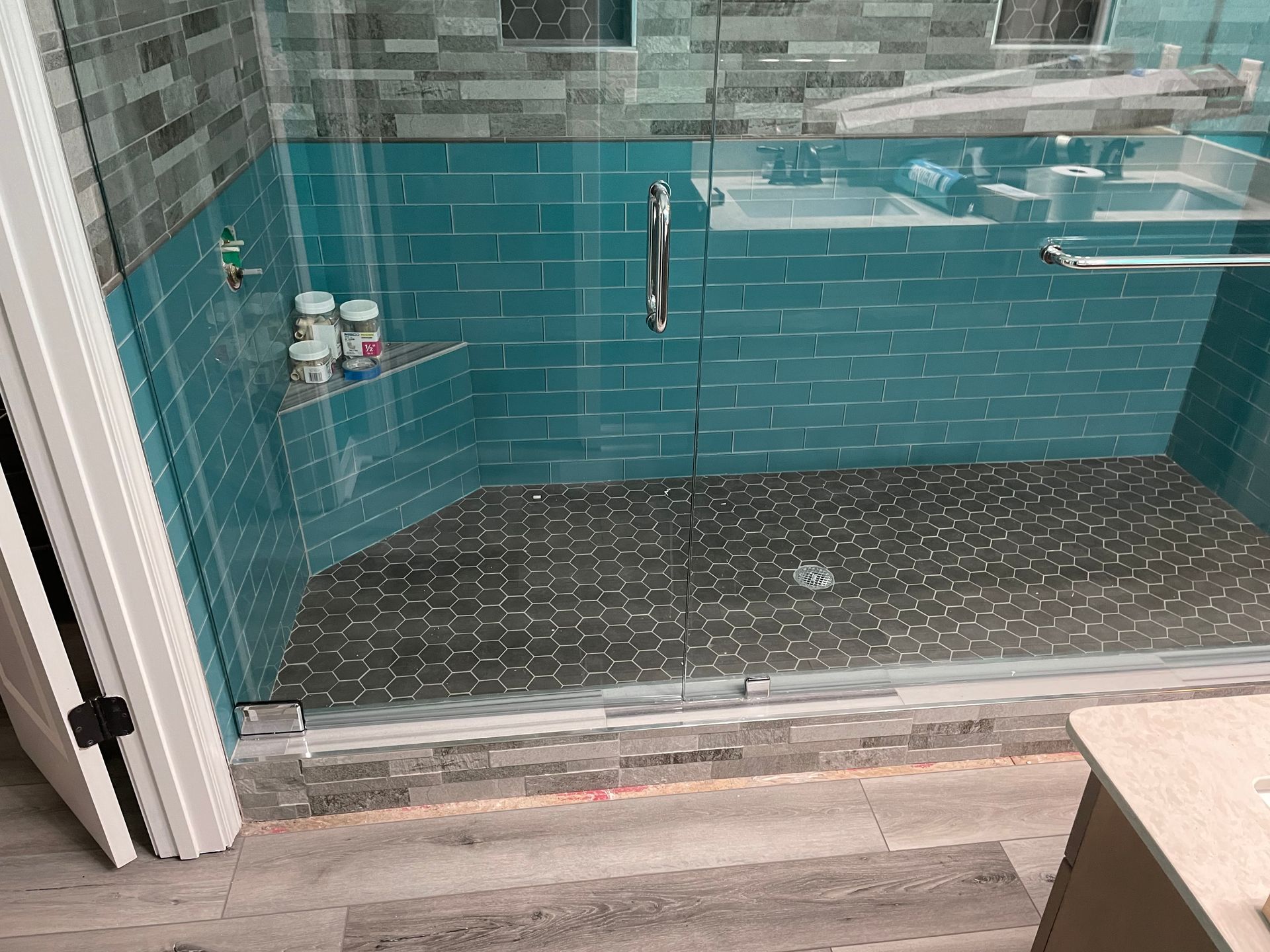 Blue-tiled shower with glass door, hexagon floor, and chrome handle in a bathroom.