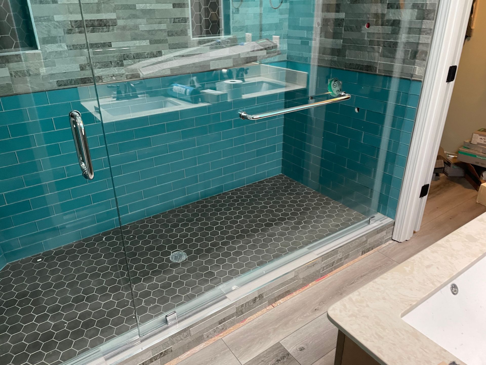 Glass walk-in shower with teal tile walls, pebble floor, and chrome grab bars