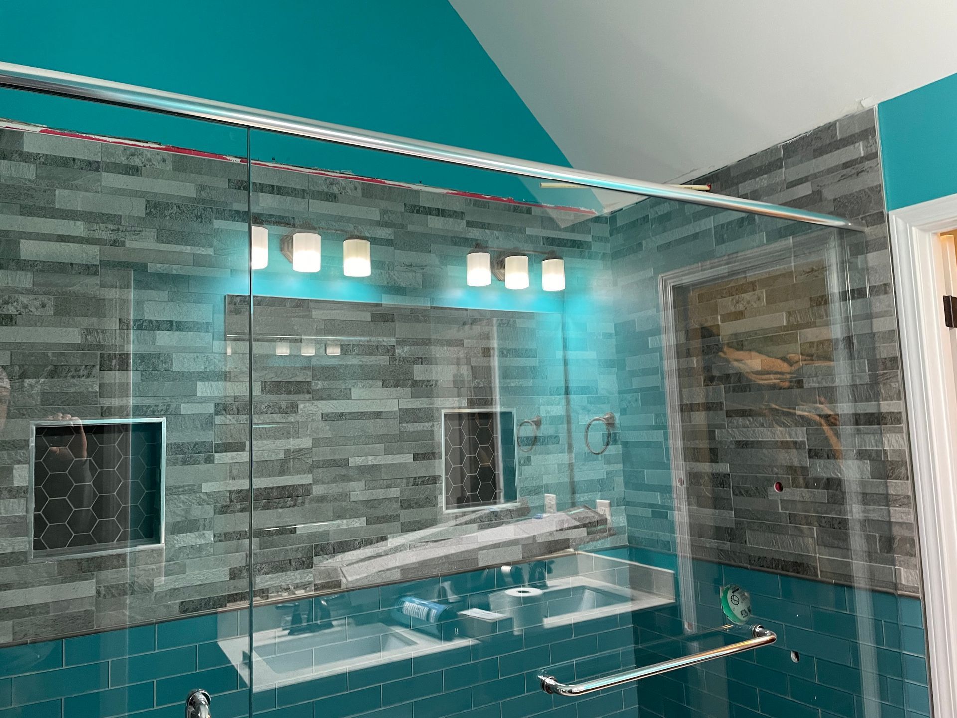 Modern bathroom with gray stone tile, teal accents, double sinks, and a large mirror