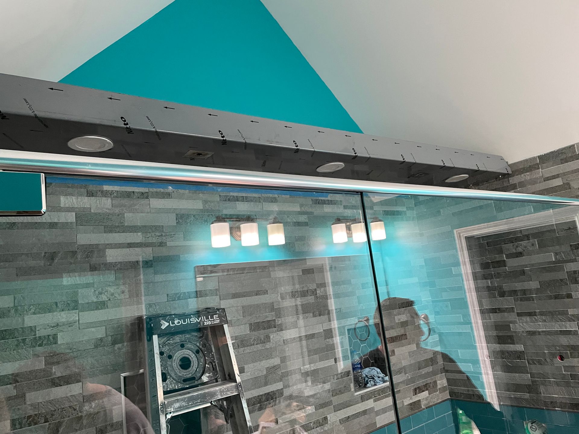 Tiled bathroom with a glass shower enclosure, chrome fixtures, and bright ceiling lights.