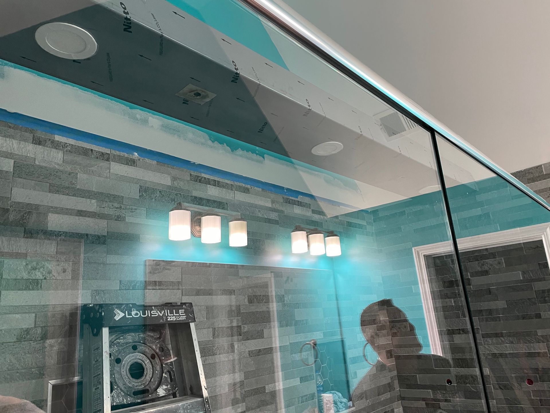 Modern bathroom with glass shower, blue accent lighting, and a person reflected in the mirror