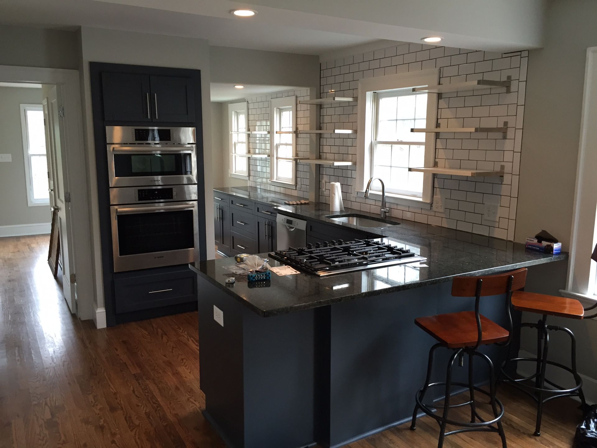 Modern kitchen with dark island, built-in ovens, tiled backsplash, and two barstools