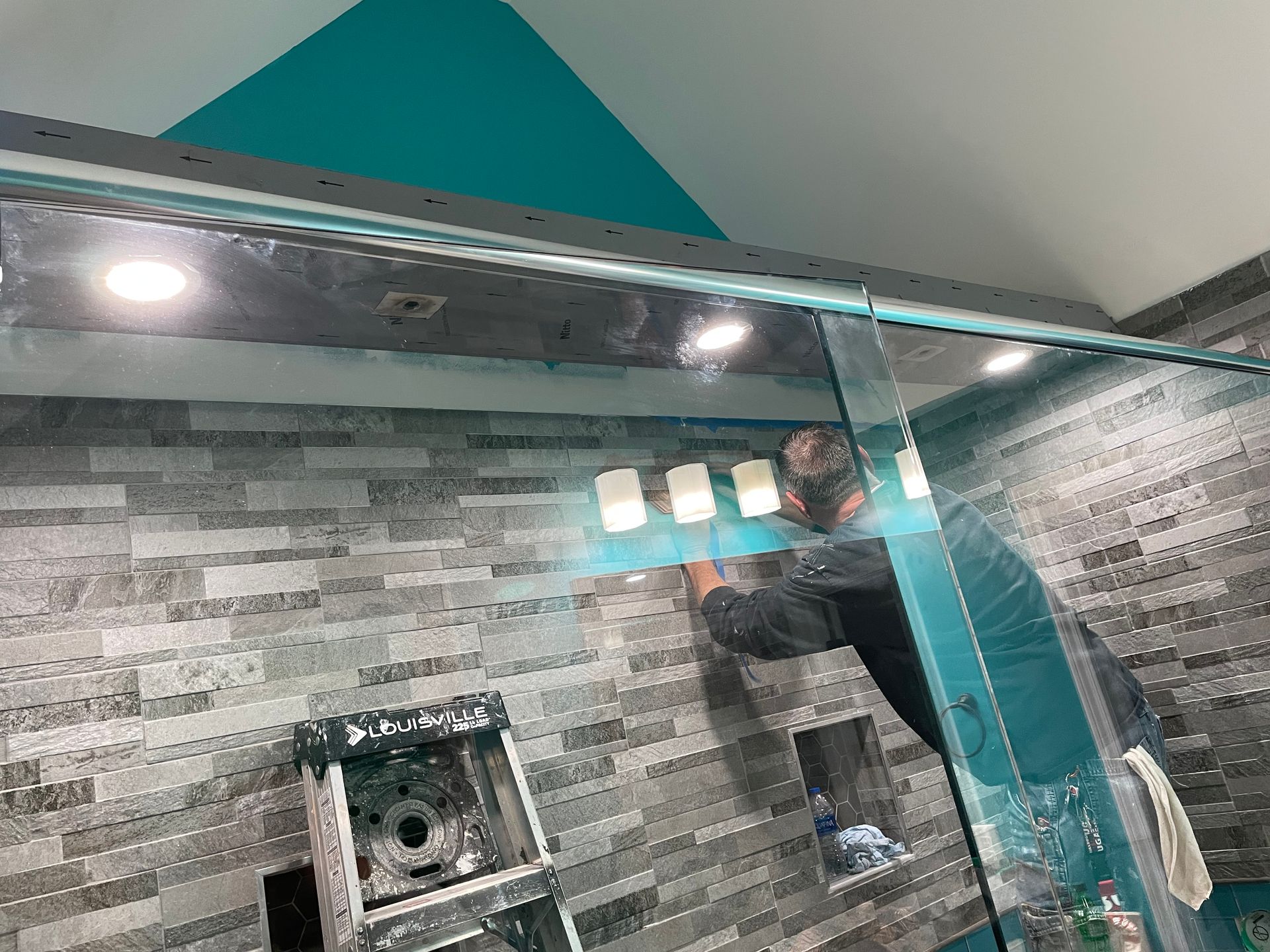 Bathroom shower with gray tile walls, glass door, and lit ceiling lights