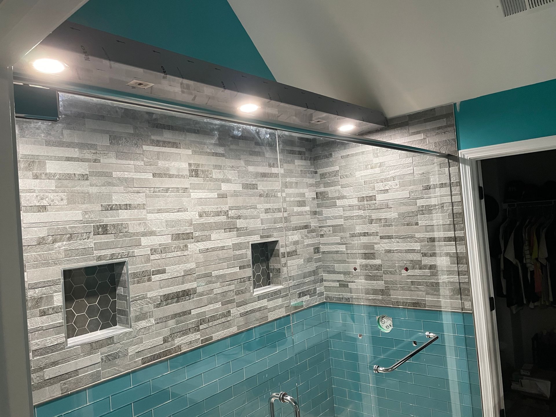 Modern tiled shower wall with recessed niches and a metal grab bar under teal accent trim