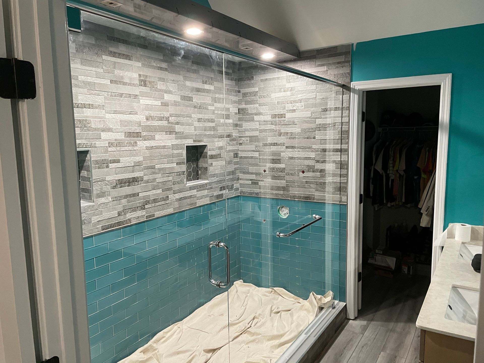 Bathroom with tiled walk-in shower, teal accent wall, and a white towel on the floor.