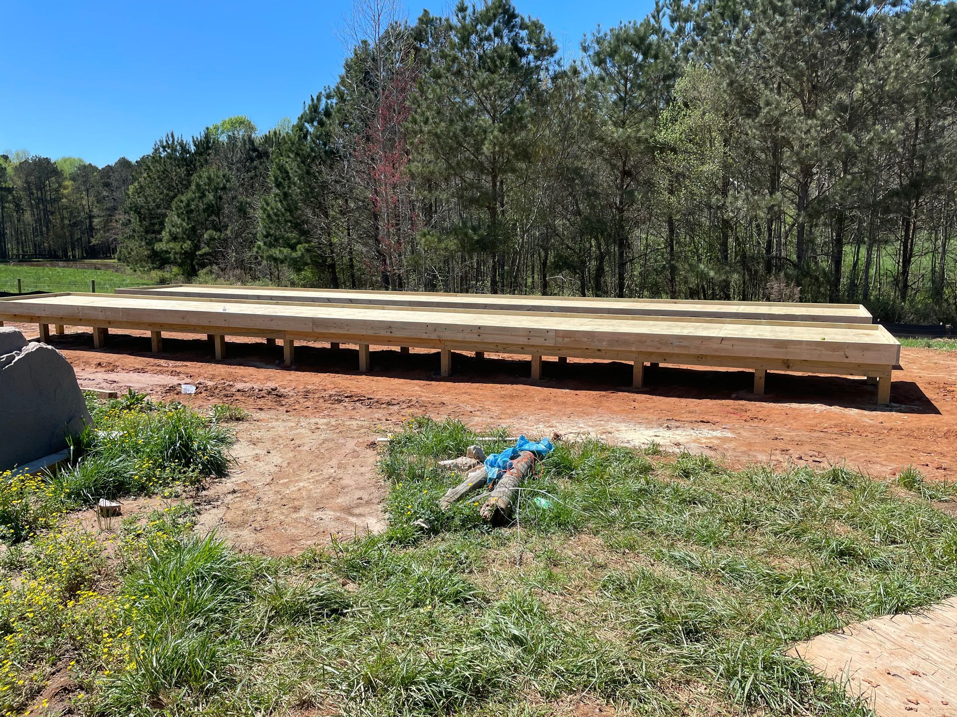 Wooden deck platform on a dirt lot beside trees, with a blue hose in the foreground.