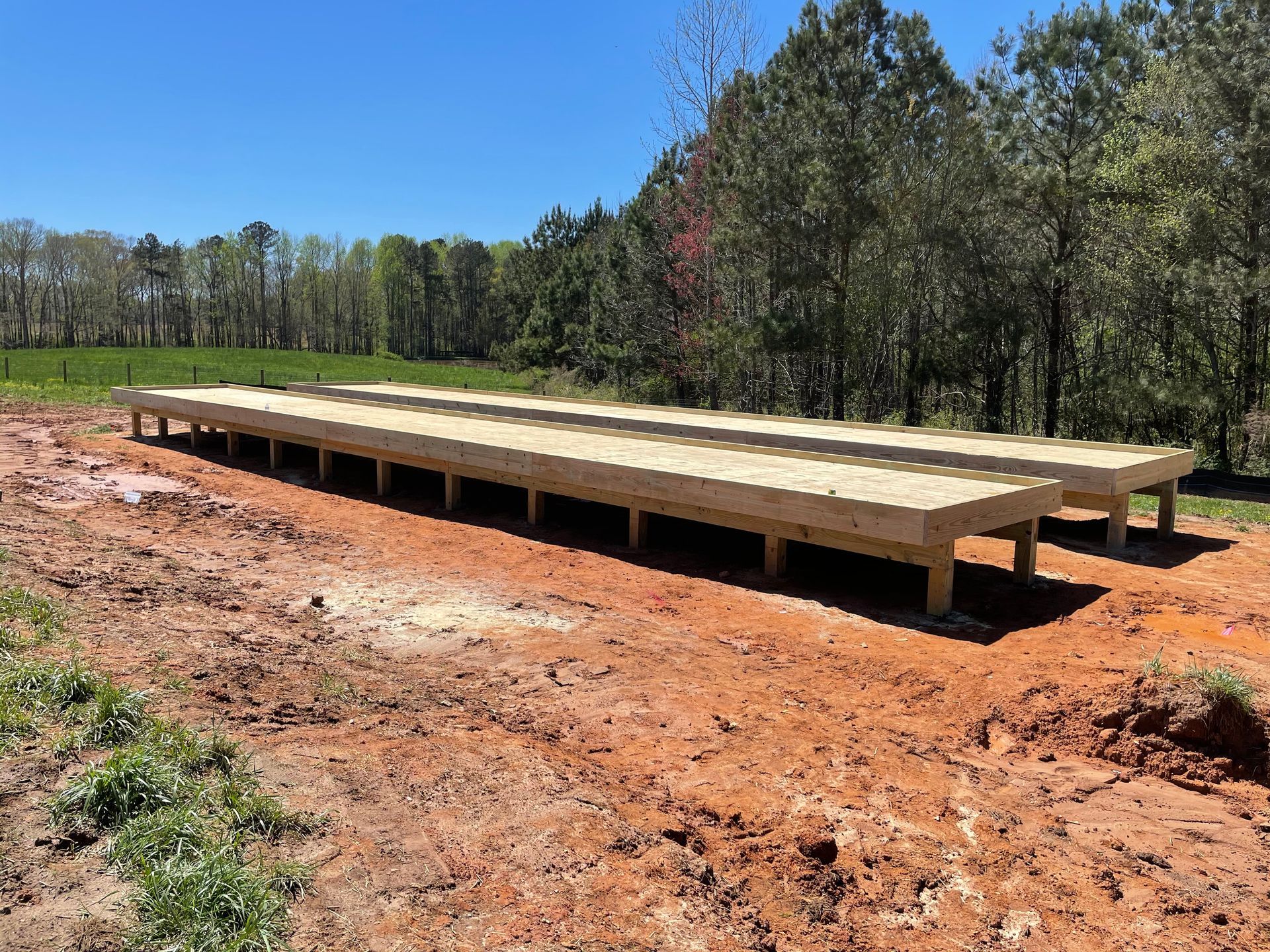 Raised wooden platform in a muddy clearing beside a forest under a blue sky