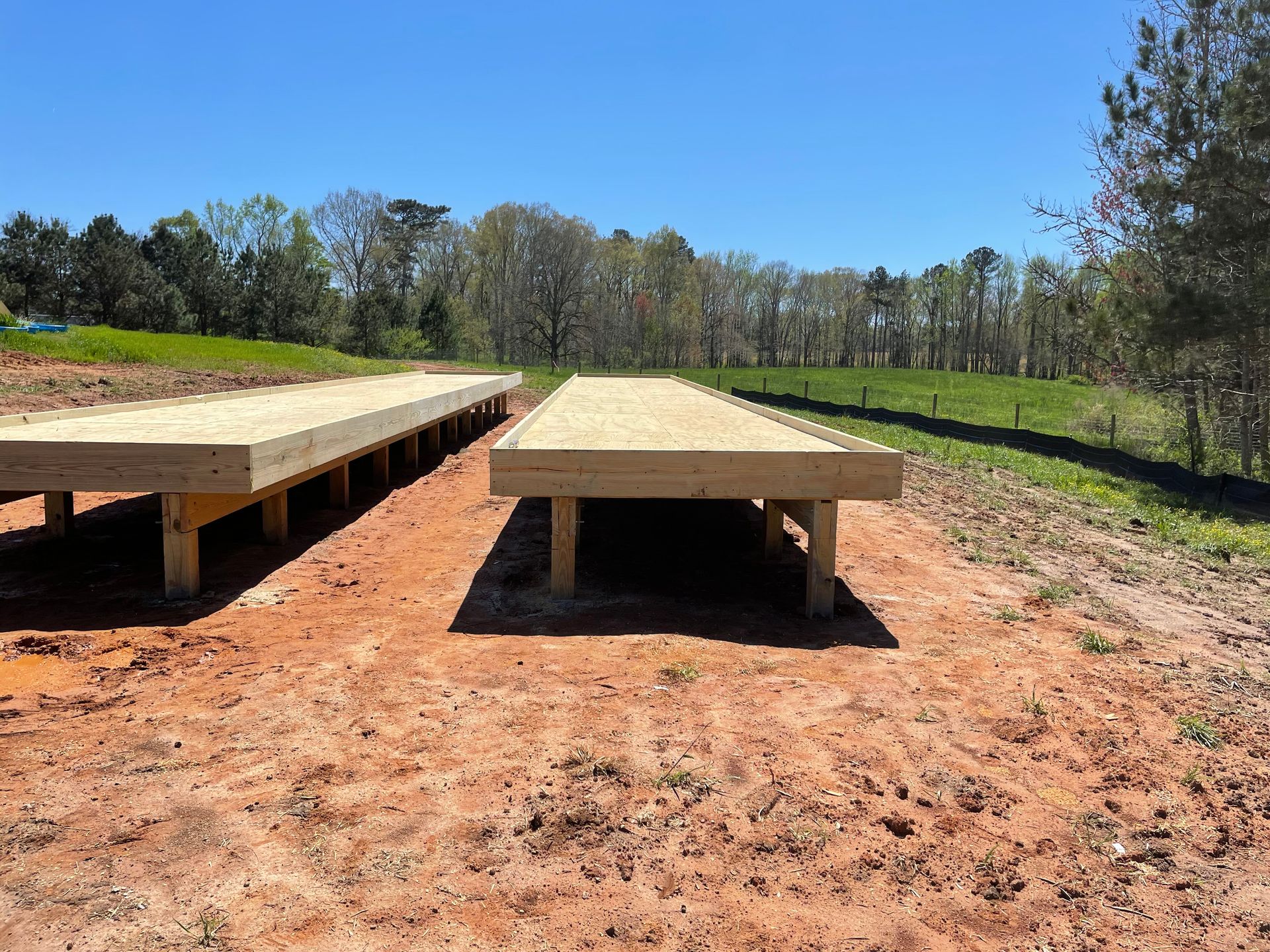 Two wooden benches on a dirt clearing under a blue sky, with trees in the background