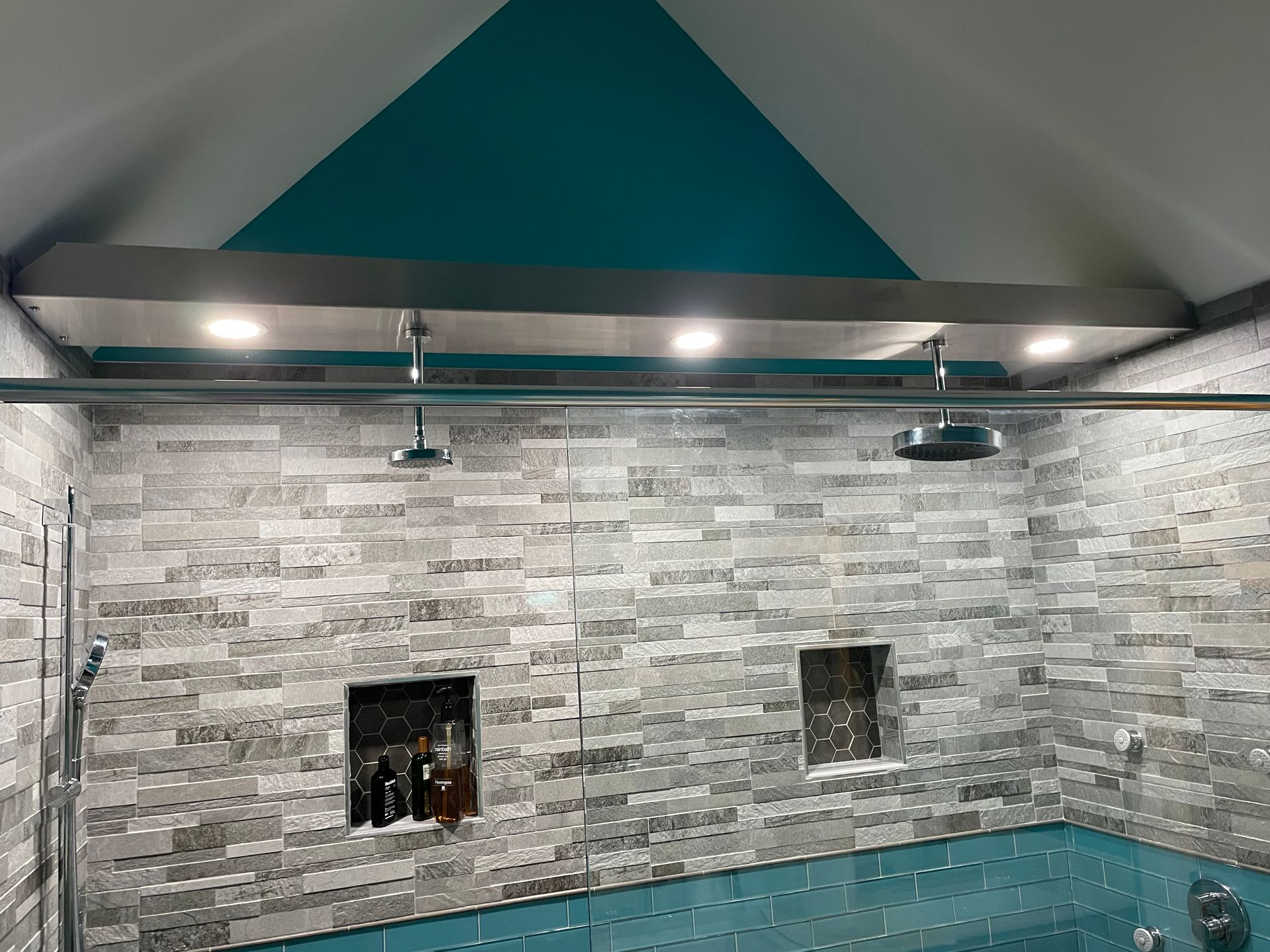 Indoor pool with gray stone walls, teal ceiling accent, and wall lights above tiled waterline.