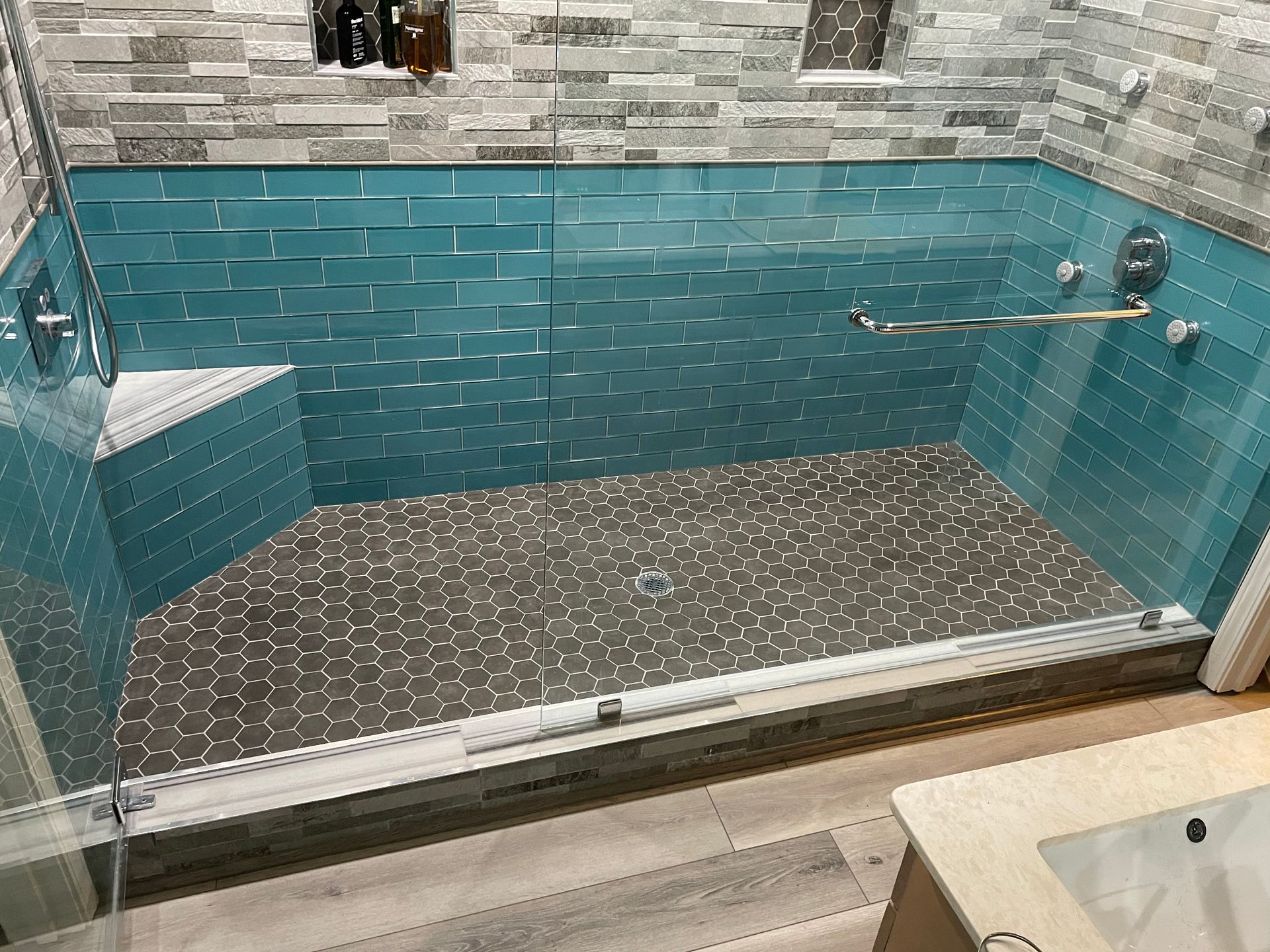 Tiled walk-in shower with glass door, turquoise wall tiles, and metal grab bars.