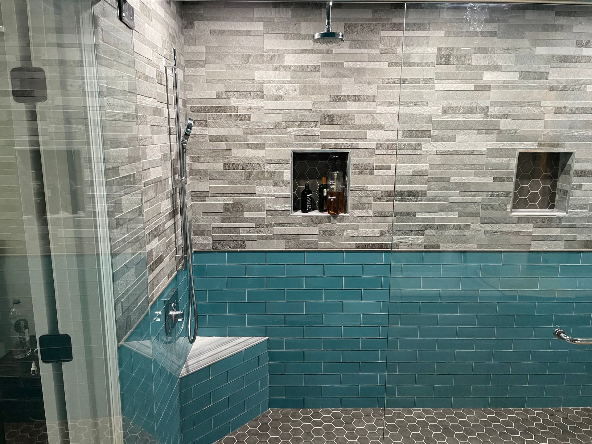 Glass shower with teal tiles and stone wall, seen from inside a bathroom