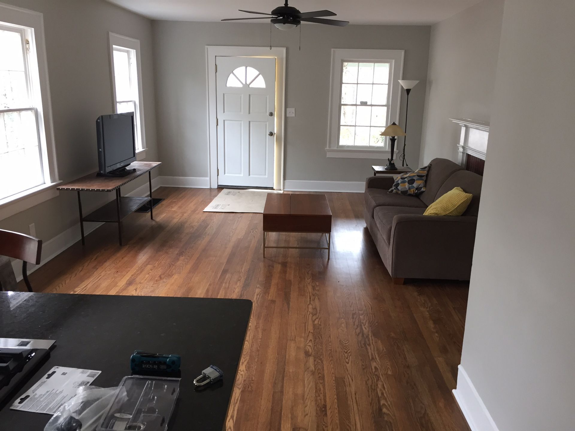 Living room with hardwood floors, gray sofa, TV, coffee table, and front door with windows