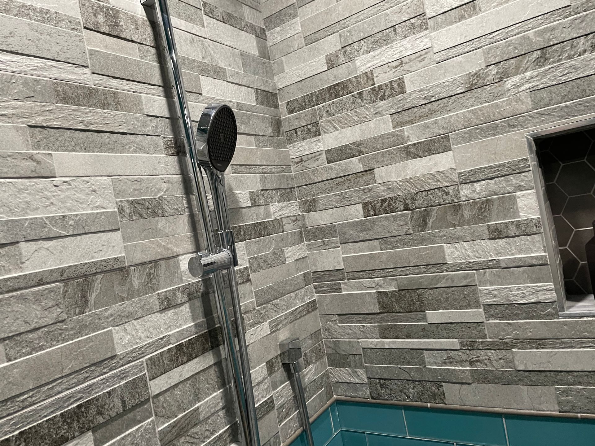 Shower corner with gray tile walls, a showerhead, and a small window
