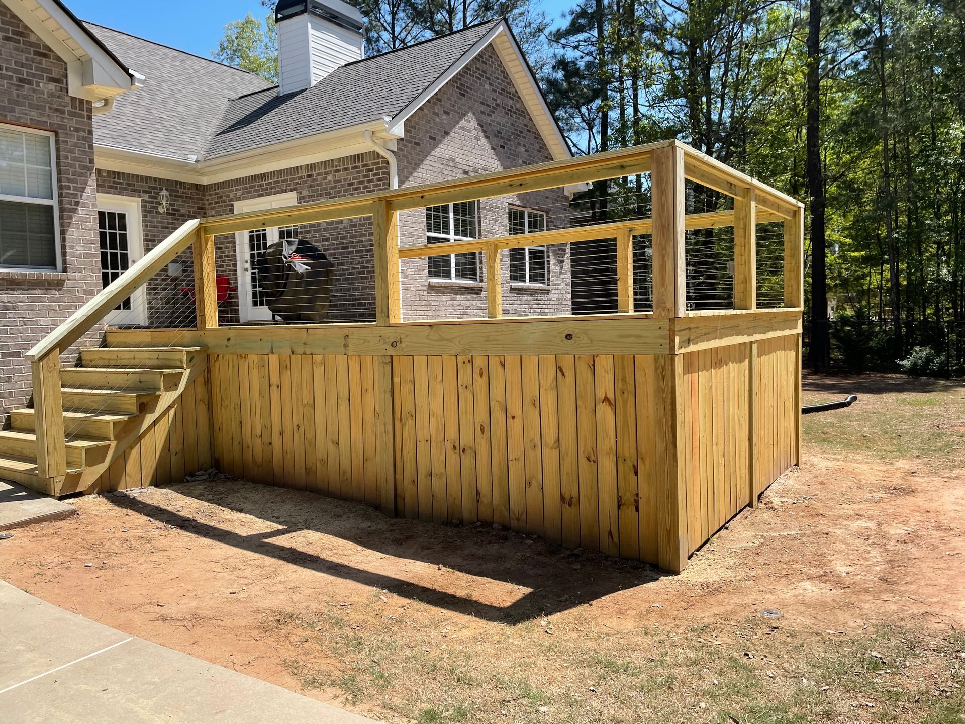 Wooden backyard deck under construction beside a house, with stairs and railing framing the platform.