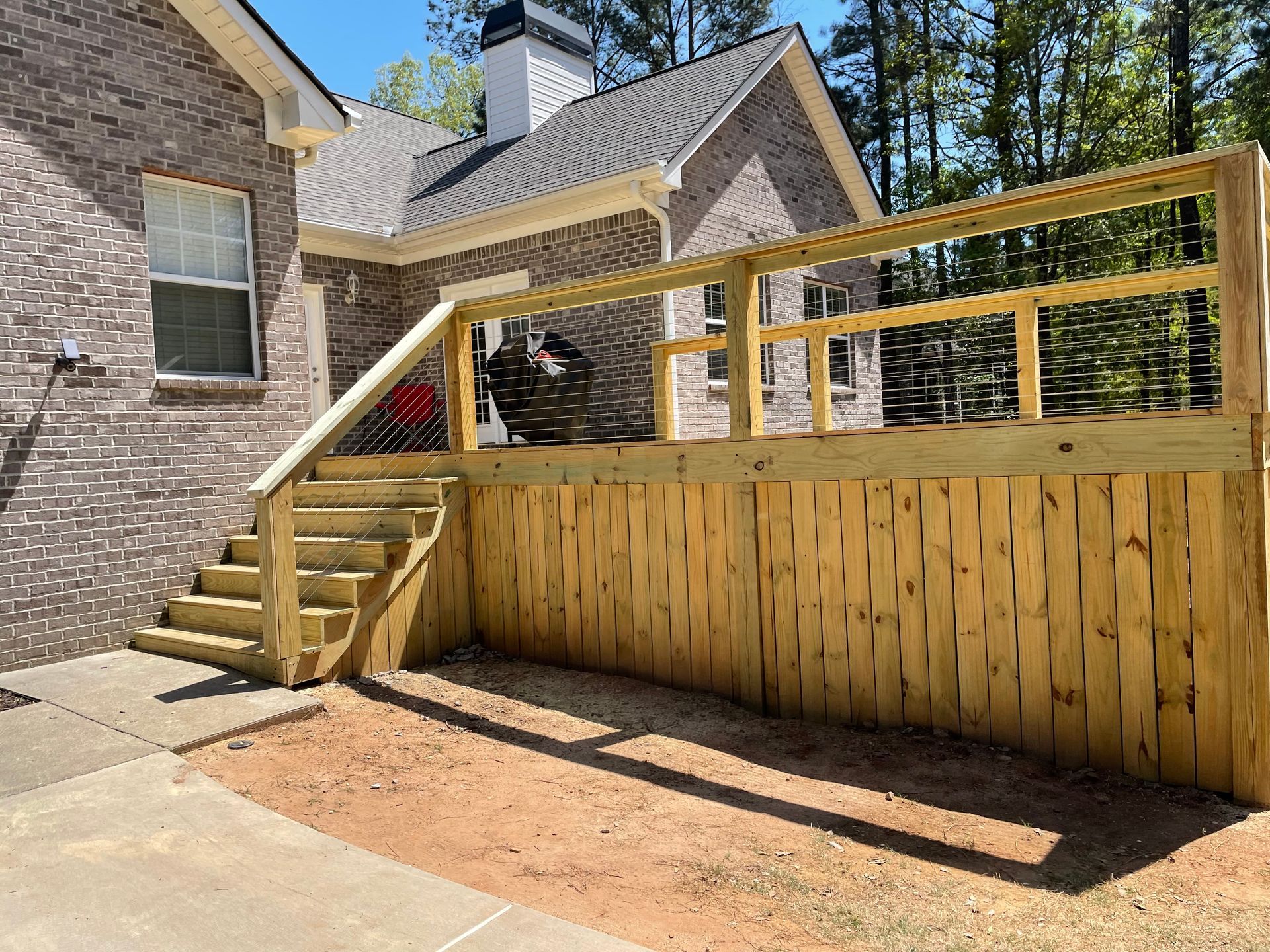 Wooden deck and stairs attached to a brick house in a sunny backyard