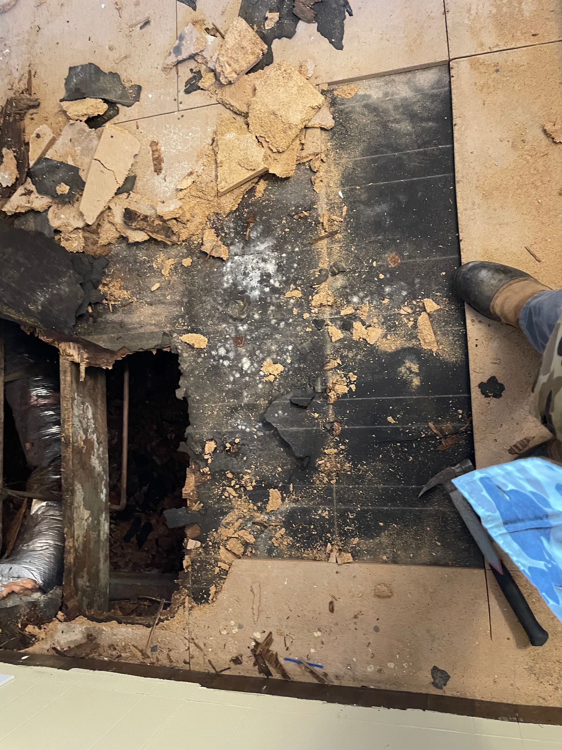 Blackened floor area with soot, debris, and damaged cardboard or insulation near a blue object.