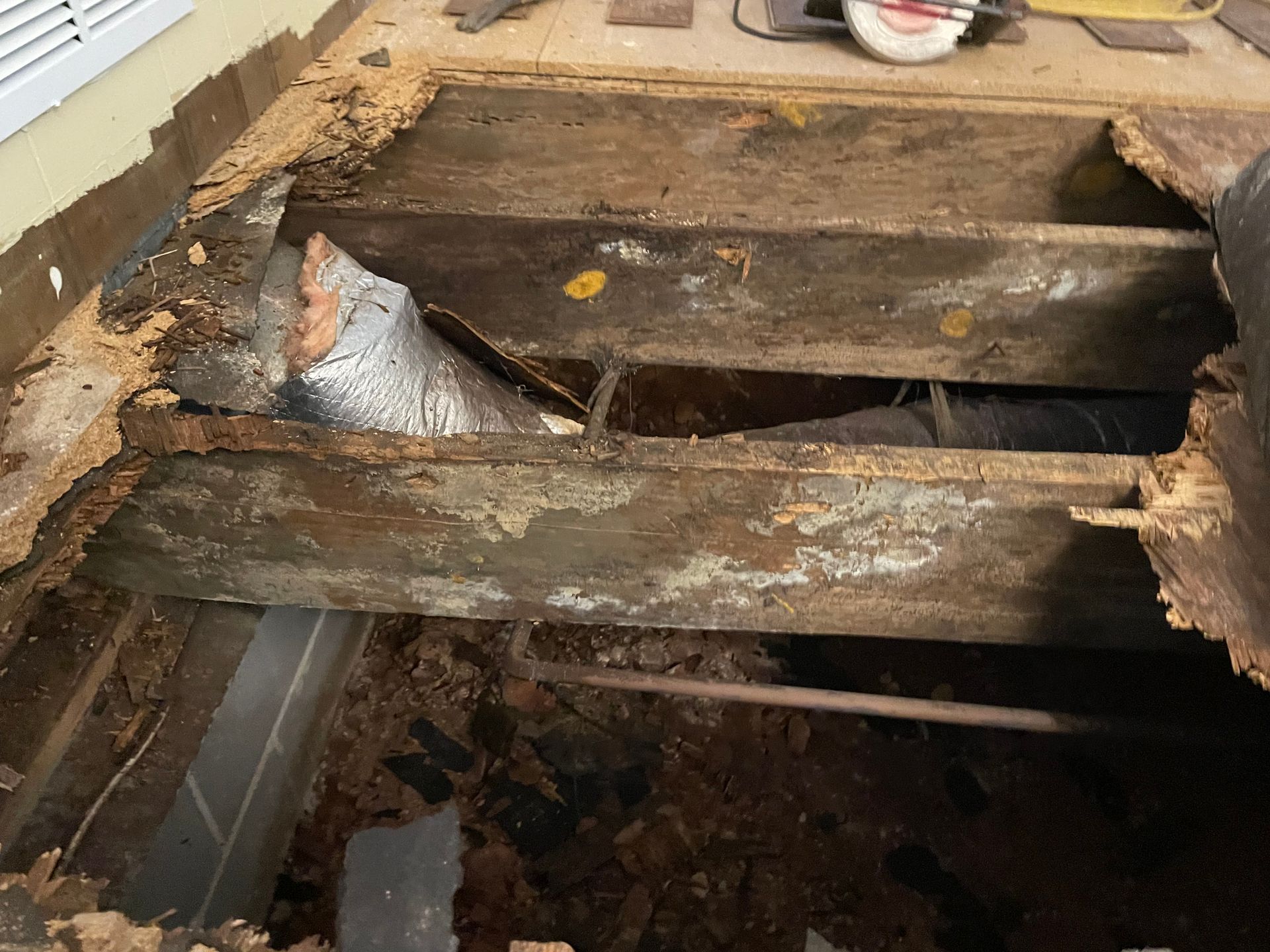 Damaged wooden floorboards with a large hole exposing joists and debris beneath
