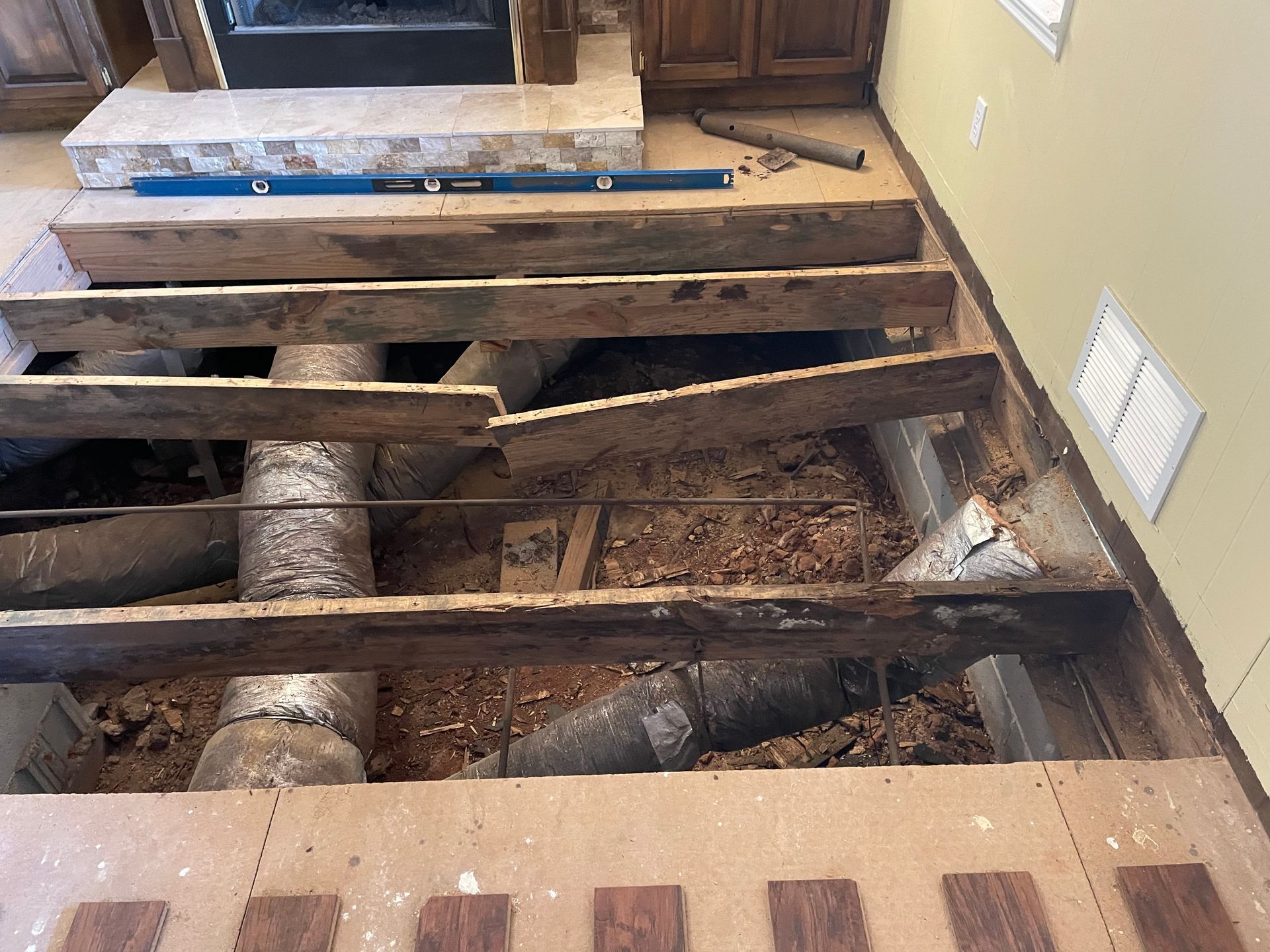 Exposed floor joists and ductwork in a room under renovation, with removed subfloor boards.