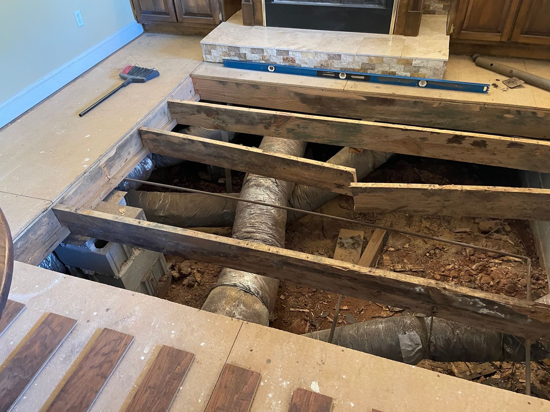 Exposed wooden floor joists and pipes in a room under renovation, with debris and insulation visible.