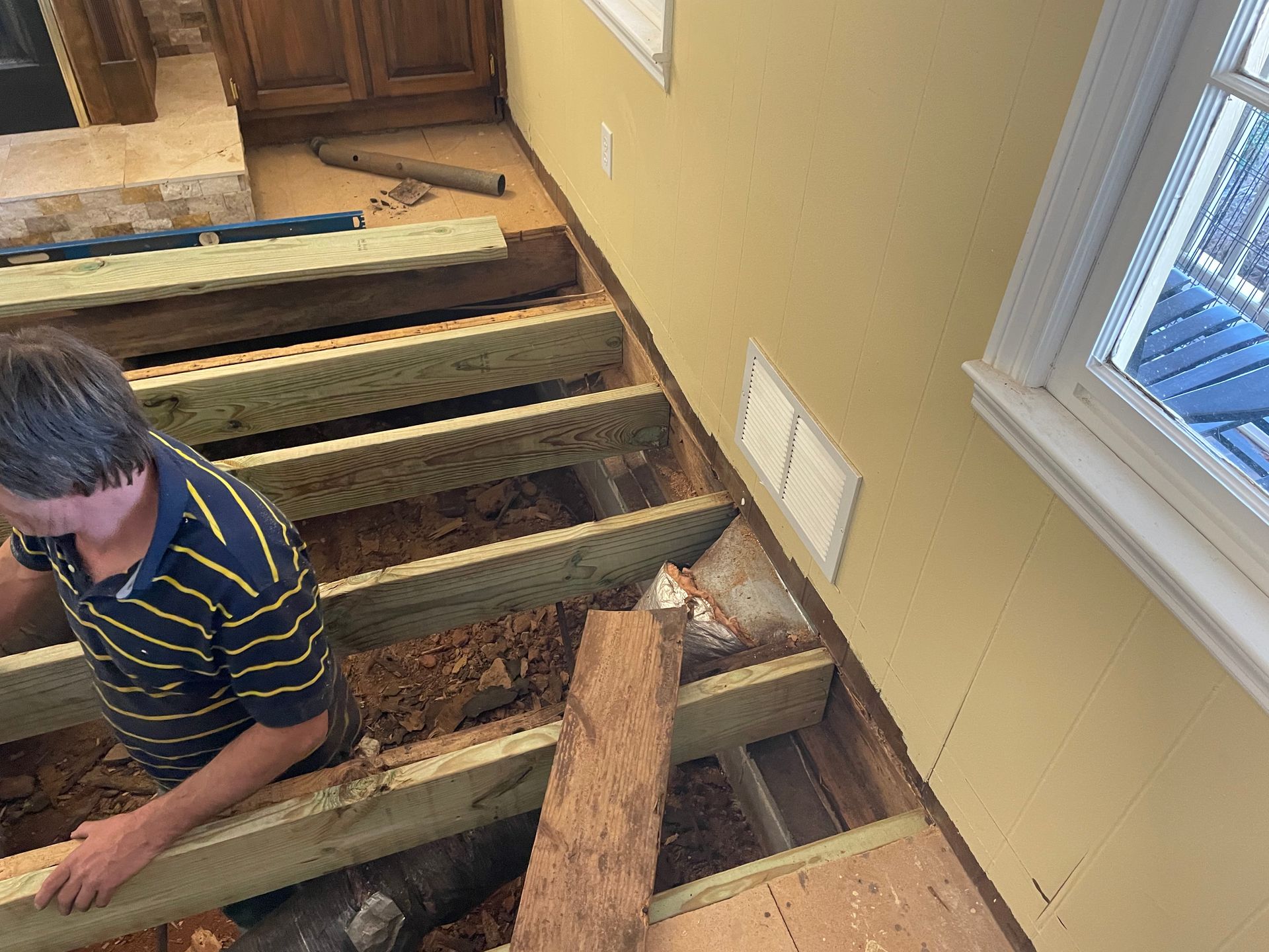 Man removing floorboards beside an open stairwell in a yellow-walled room