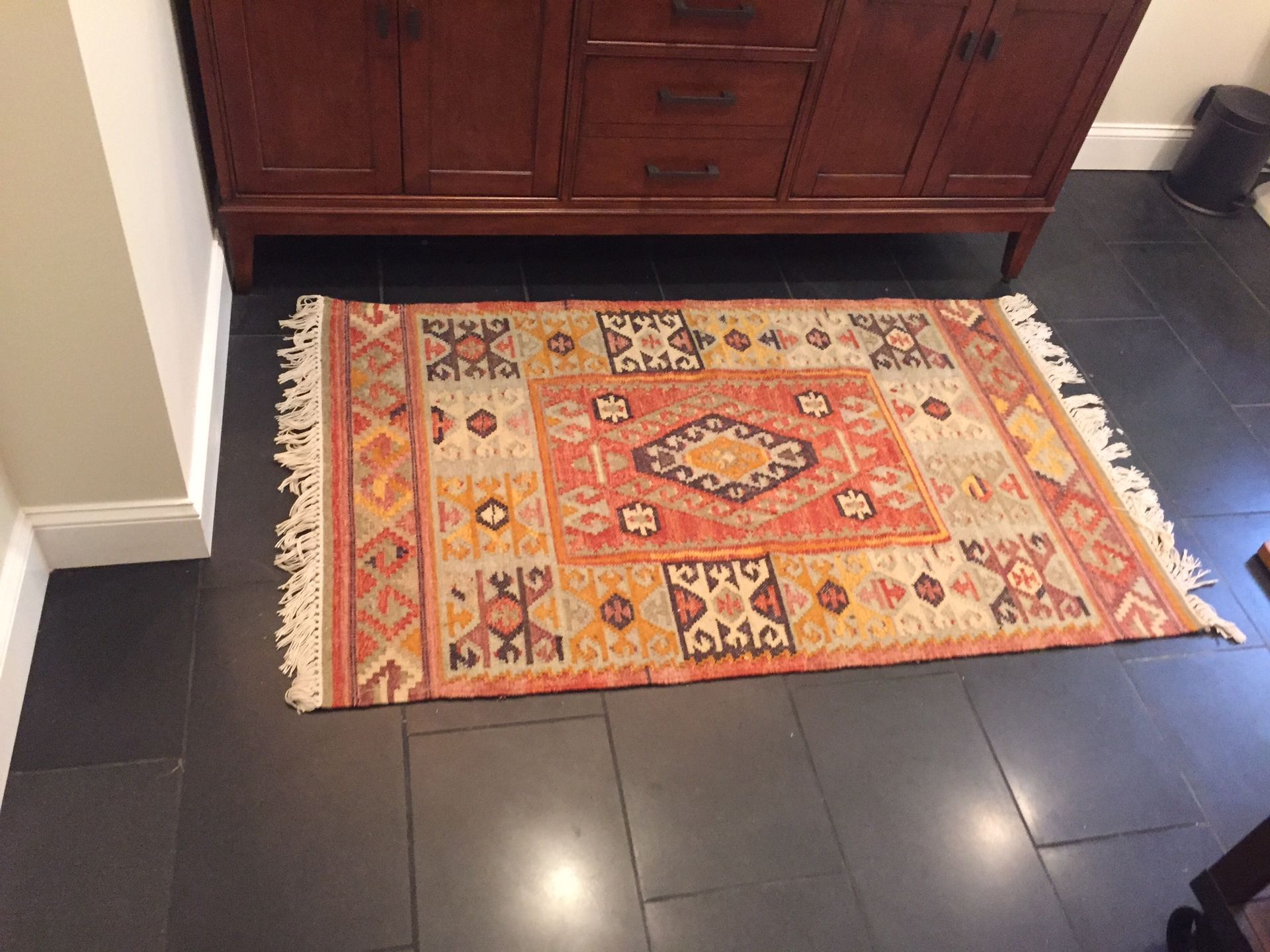 Colorful patterned rug on dark tile floor in front of a wooden cabinet