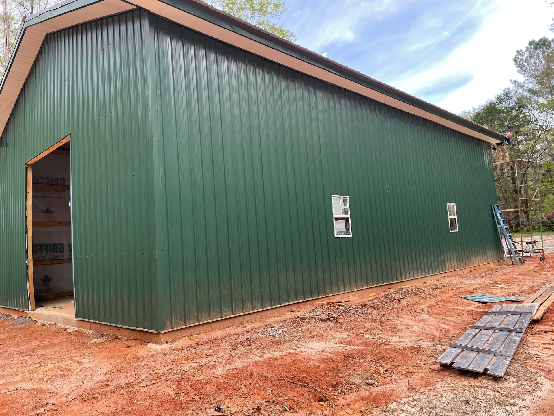 Green metal barn with an open doorway and small windows on a dirt lot