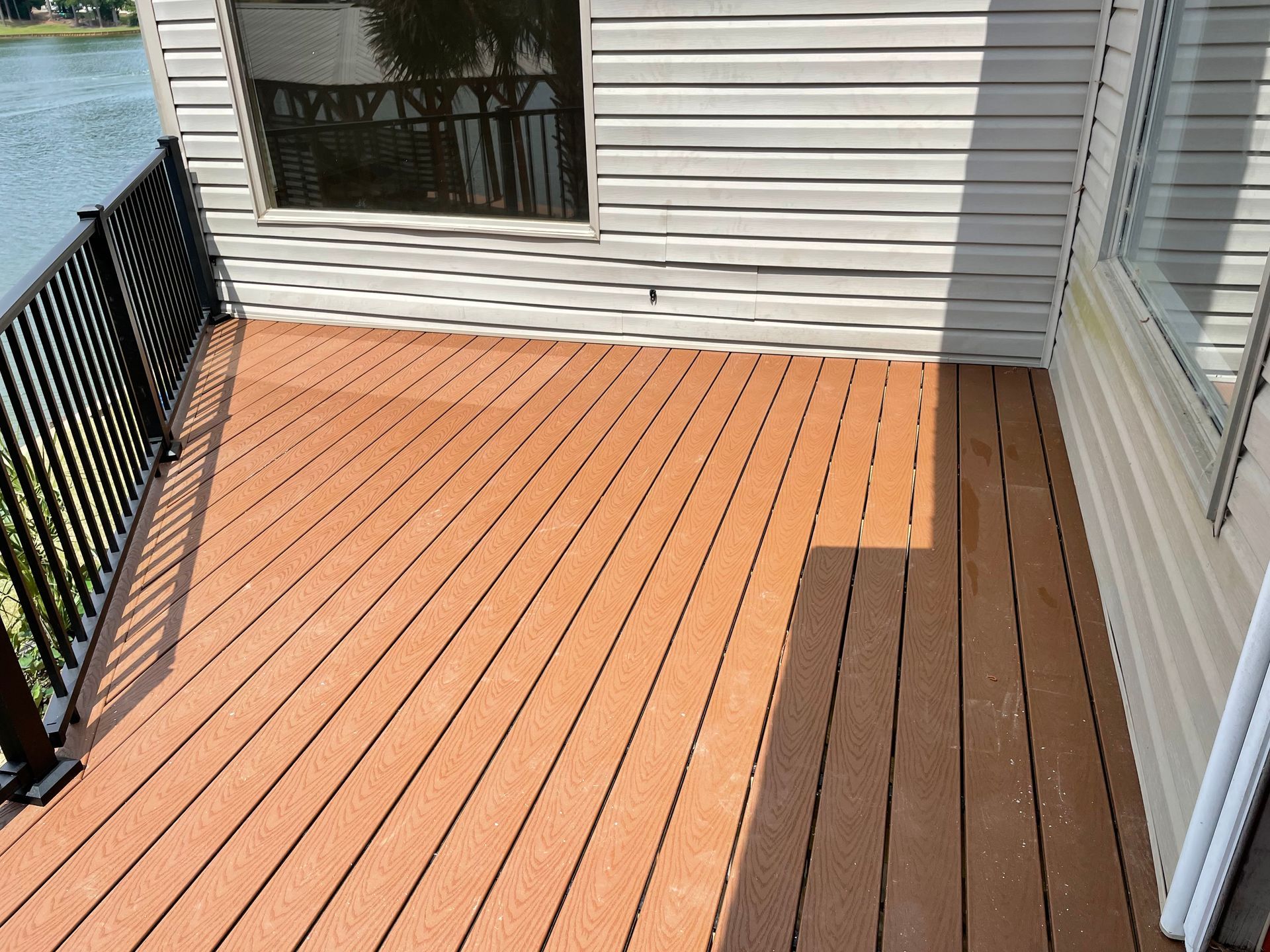 Small outdoor balcony with a black railing and light wood composite decking beside a house.