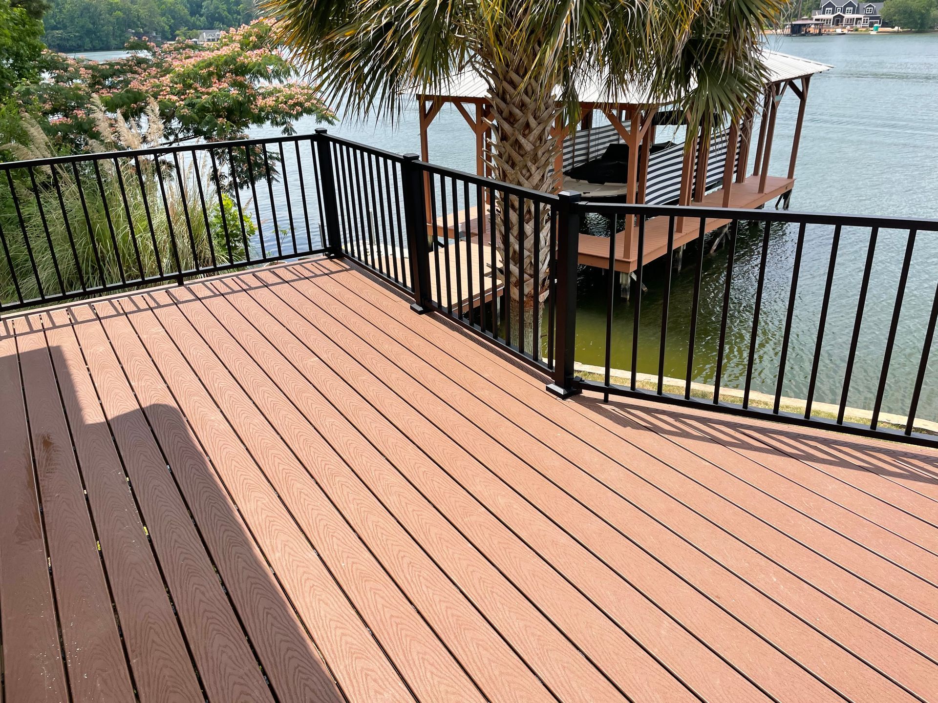 Wooden deck with black railing overlooking a lake and a dock with palm trees