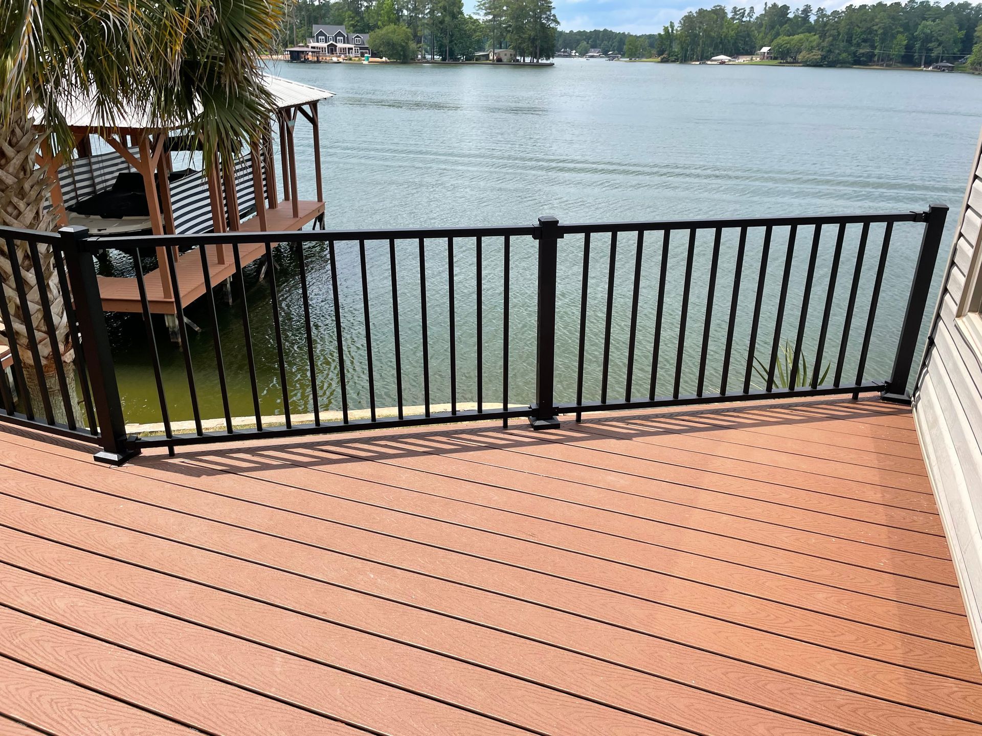 Wooden deck with black railing overlooking a calm lake and trees